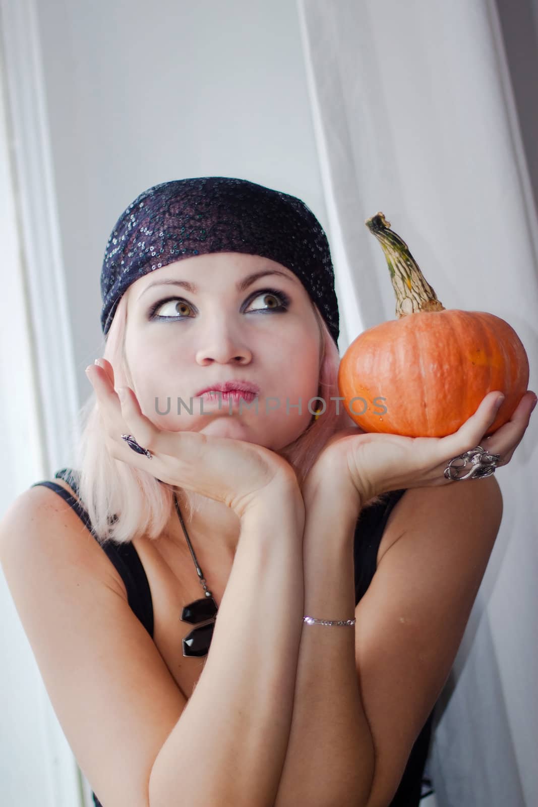 Young lady is seating on the window with small pumpkin