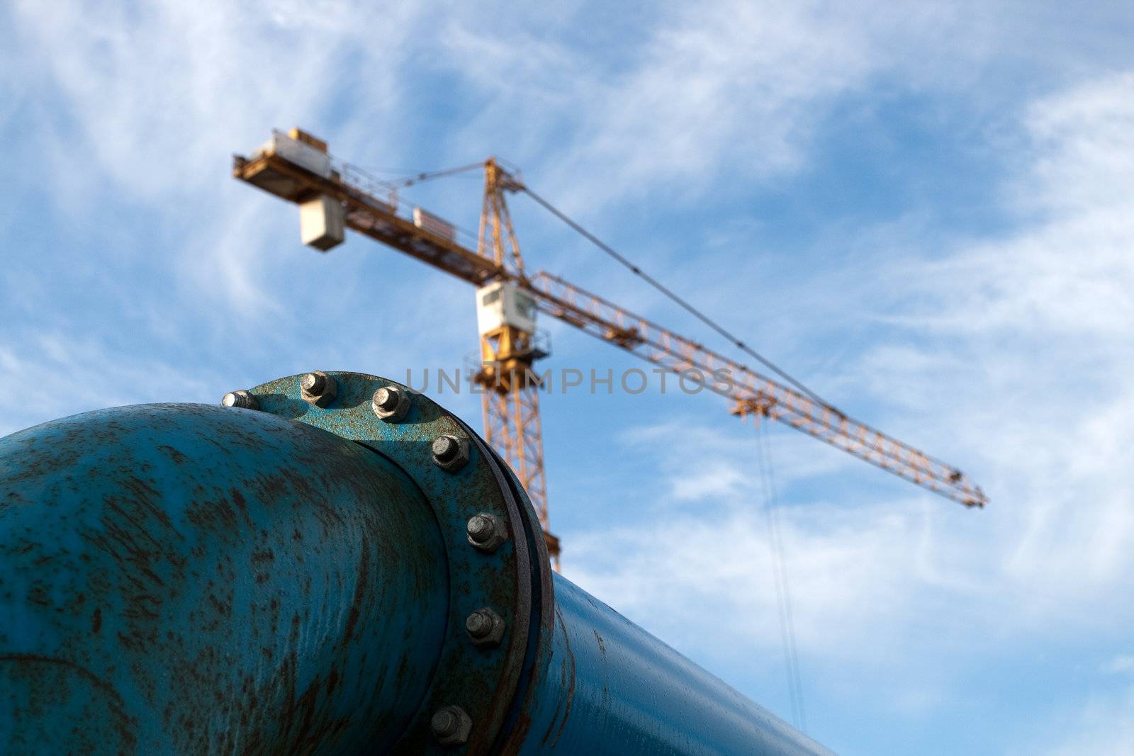 Blue pipelines with bolts at construction site with crane in background