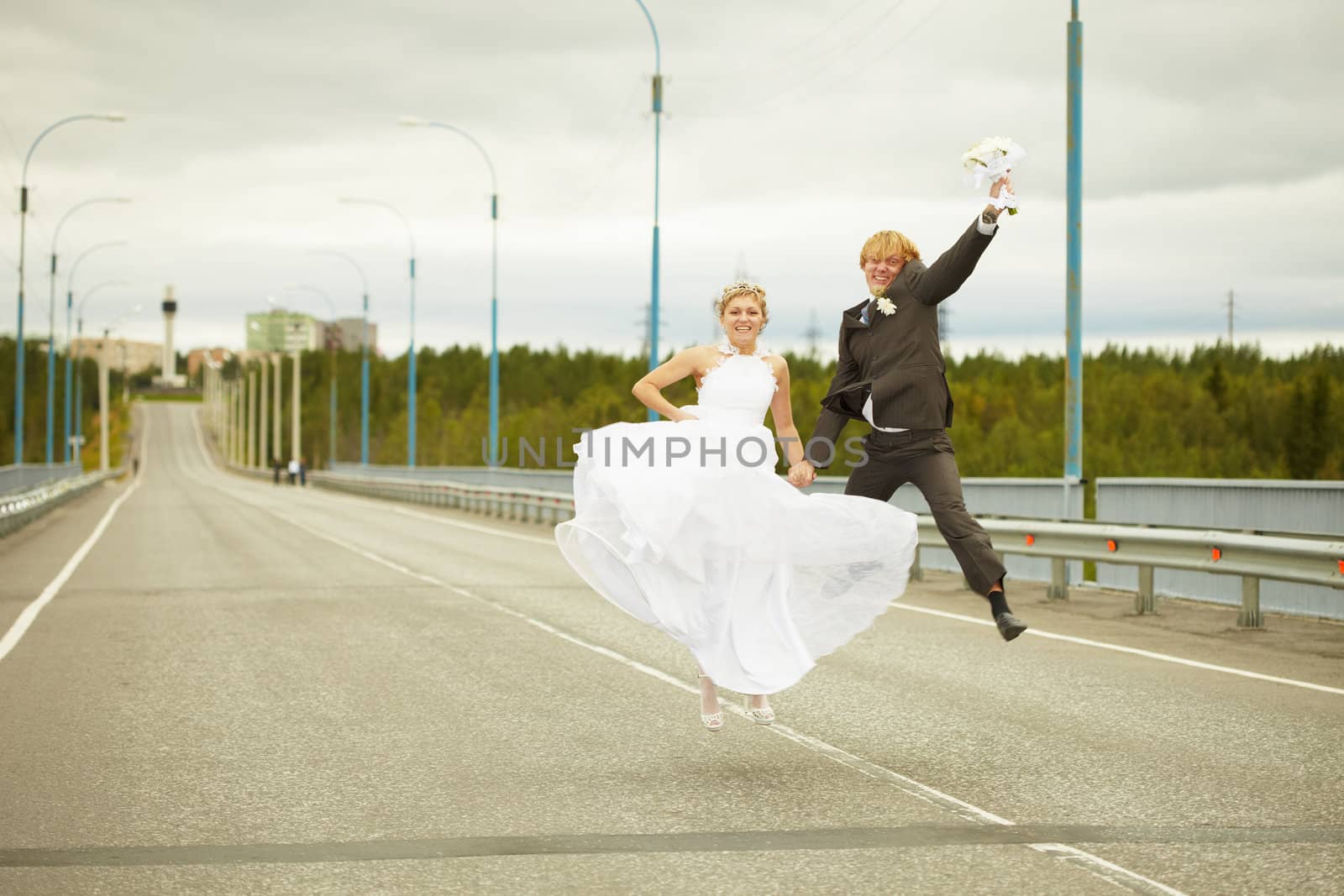 Newly married young pair cheerfully jumps on highway