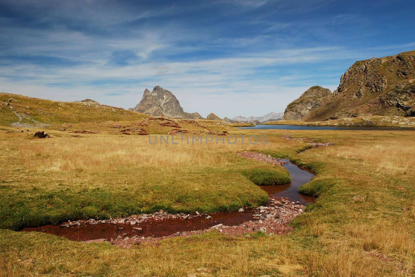 Panorama of Anayet plateau with a small stream red from rocks in Spanich Aragon and Peak du Midi d'Ossau in French Bearn in Pyrenees mountains at background,  in summer time