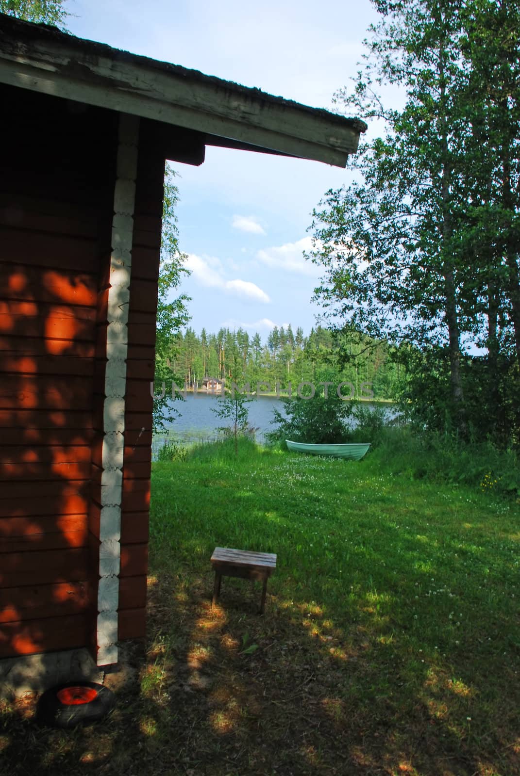 Look from the wooden house to the border of a lake in Central Finland, there are a stool and a wooden boat in the border of lake, surrounded by the forest