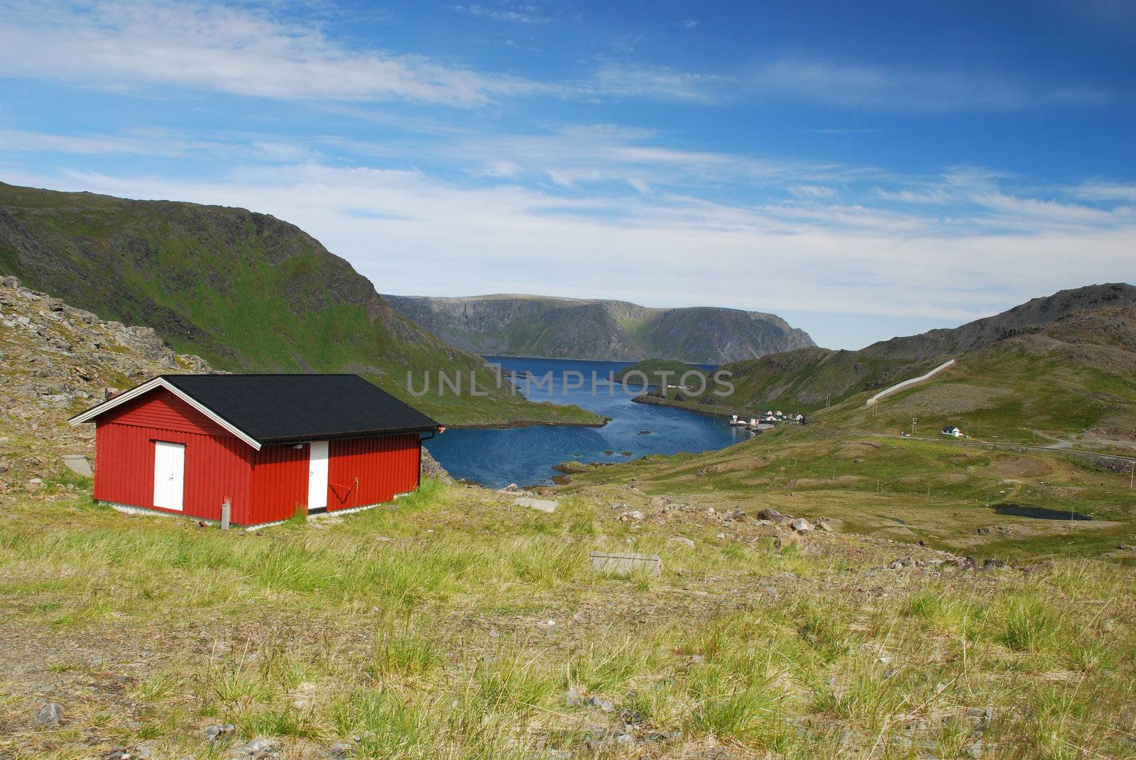 Lonely wooden house close to Nordkapp in wild nordic Mageroya Island, surrounded by tundra. Some fisher's small village and see blue surfaces are at fare background