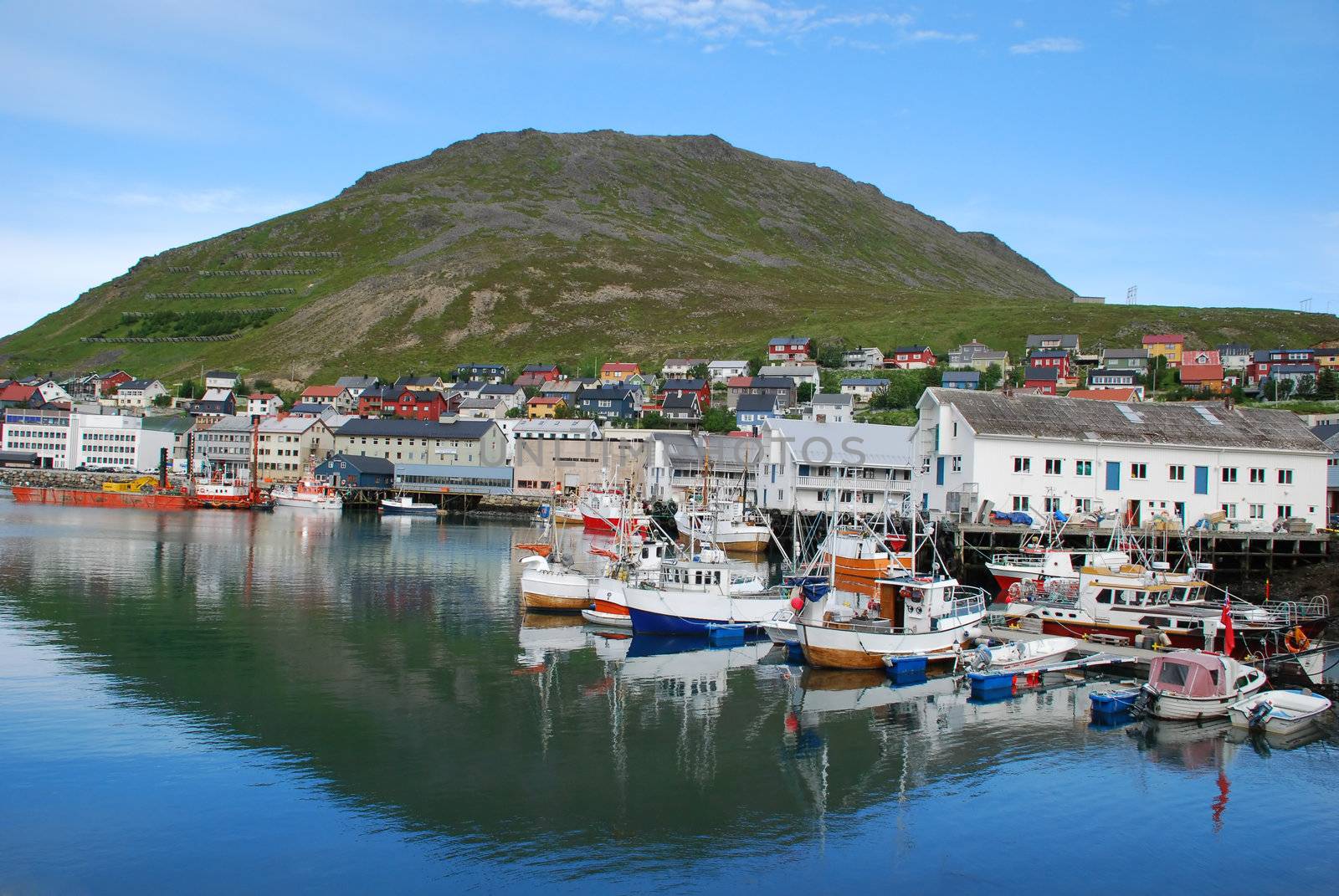 Its a port and cityscape of Honningsvag, one of the northernmost city in Norway and  in the world,  fishers and indusctrial vessels are at biggest port of Mageroya Island, with the buildings, houses and desert hill at background