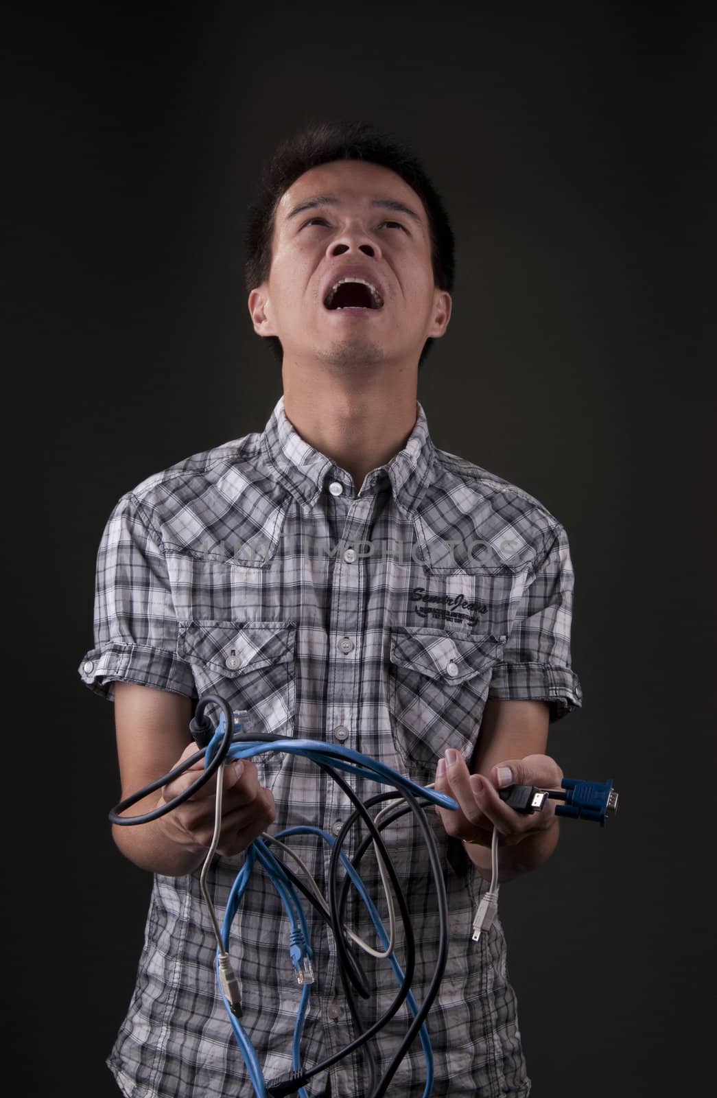 Asian man frustrated as he yells and holds various wires and cables