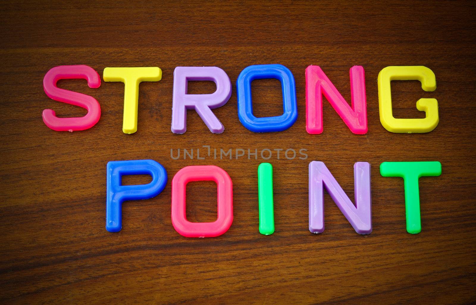 Strong point in colorful toy letters on wood background