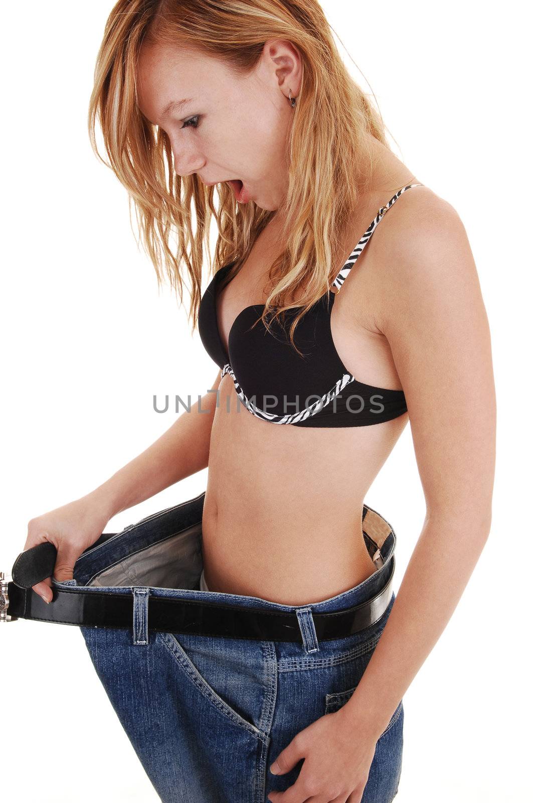 A slim teenage girl in a black bra and a very big jeans, after she last
so much weight, is very surprised, for white background.
