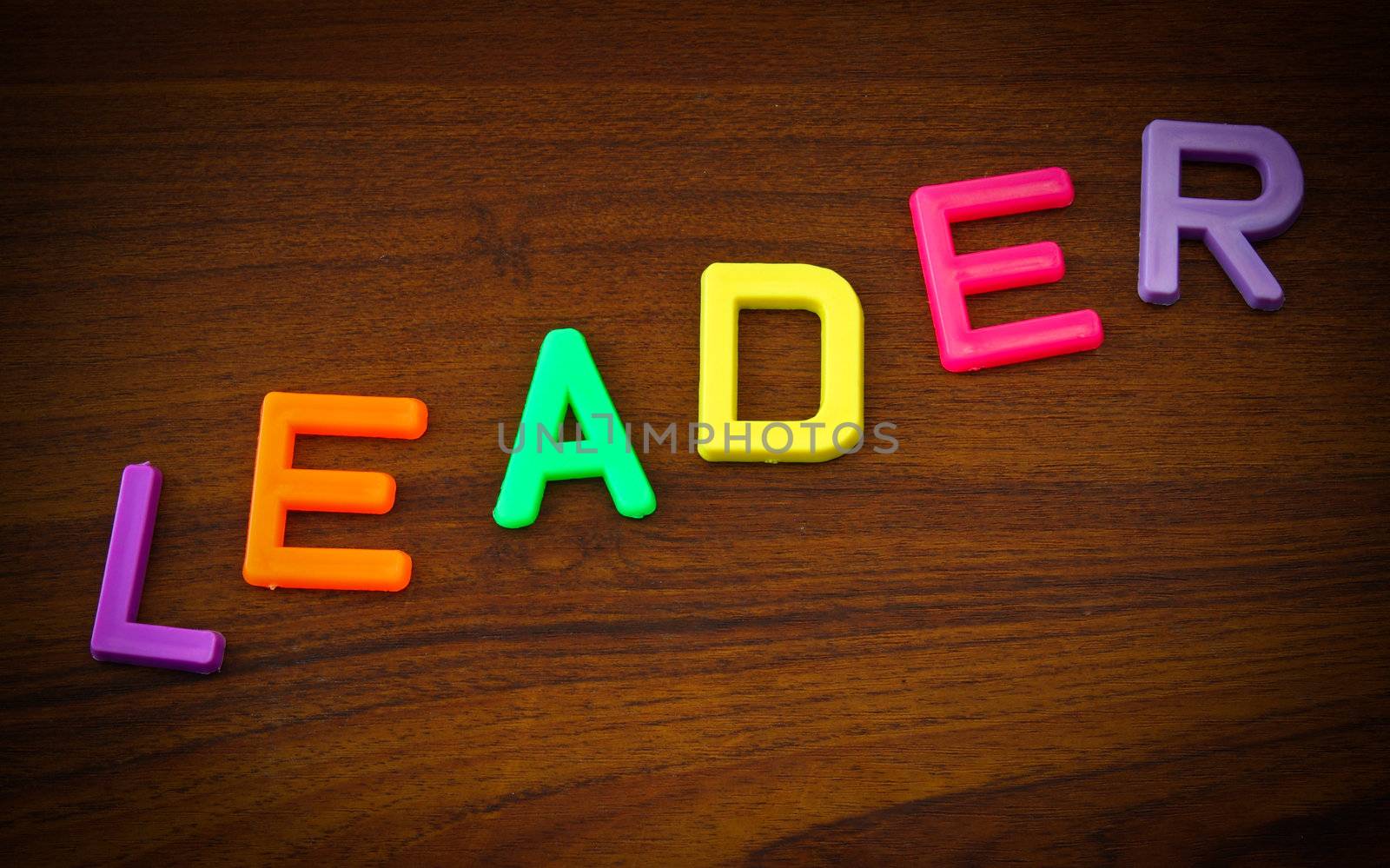 Leader in colorful toy letters on wood background