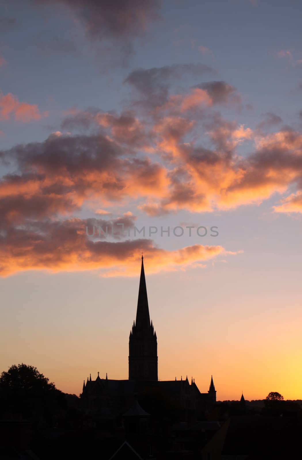 A winter sunset over Salisbury Cathedral in the city of Salisbury, Wiltshire. The cathedral silhouetted against low winter clouds. Set on a portrait format.