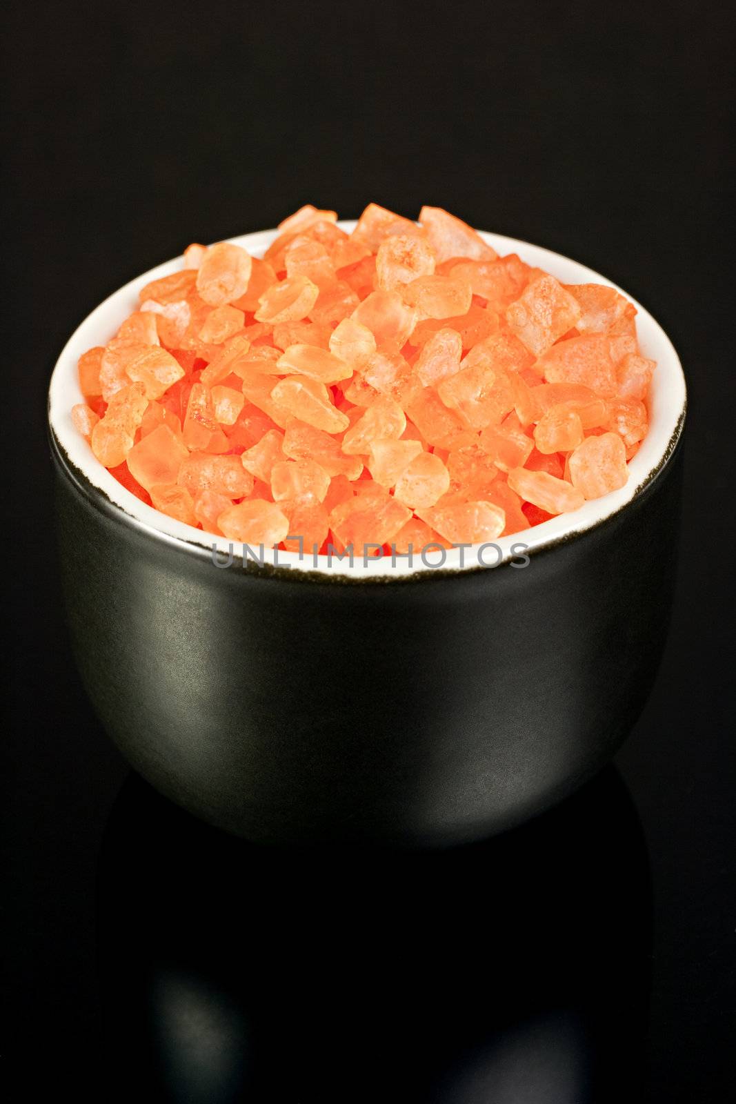 Orange bath salt black bowl on a black mirrored background.