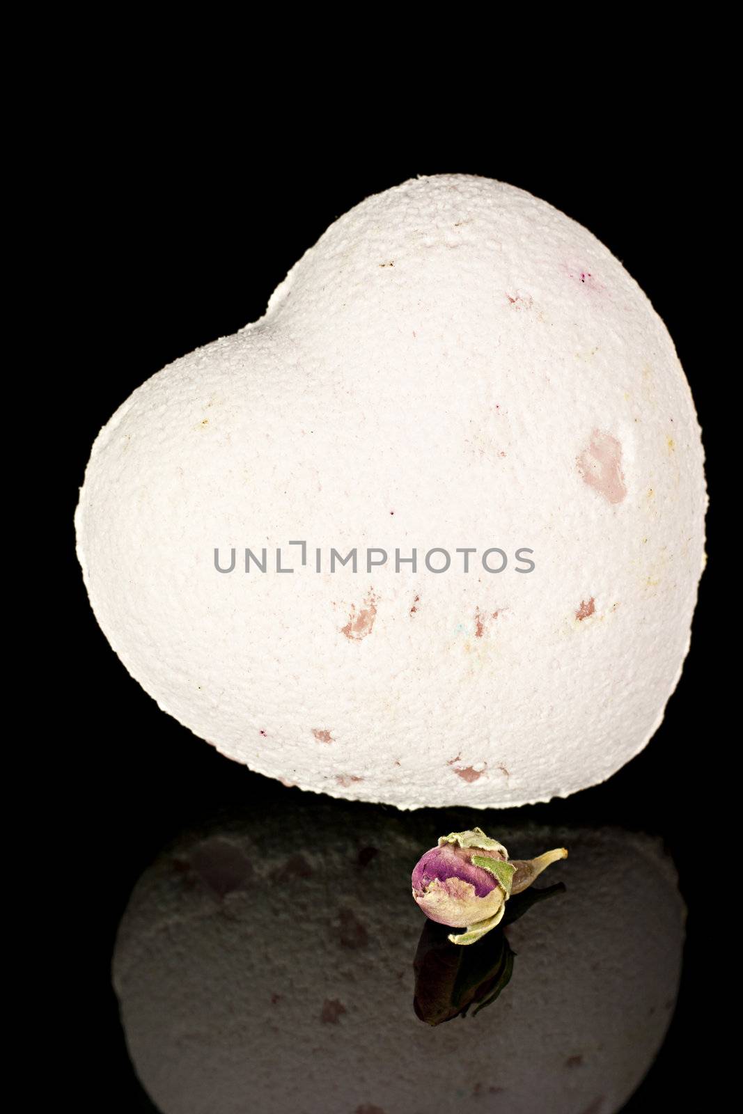 Bath salts in the form of the heart with a dry  flowers  on a black background.