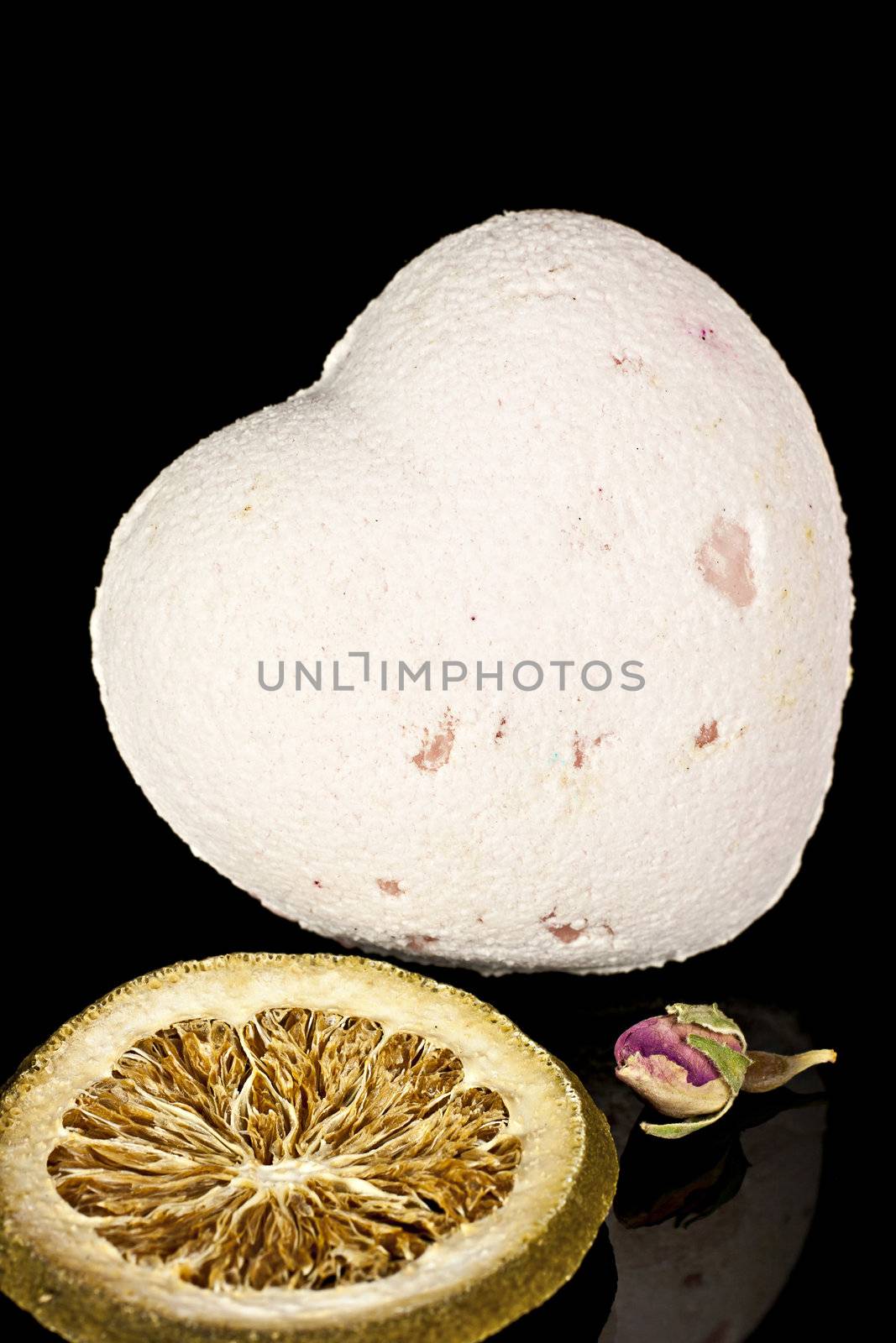 Bath salts in the form of the heart with a dry flowers and the dried slices of lemon on a black background.