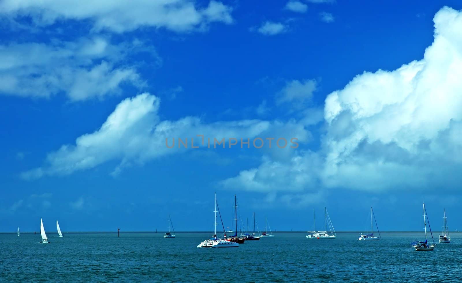 several anchoring sailboats; blue sky and water