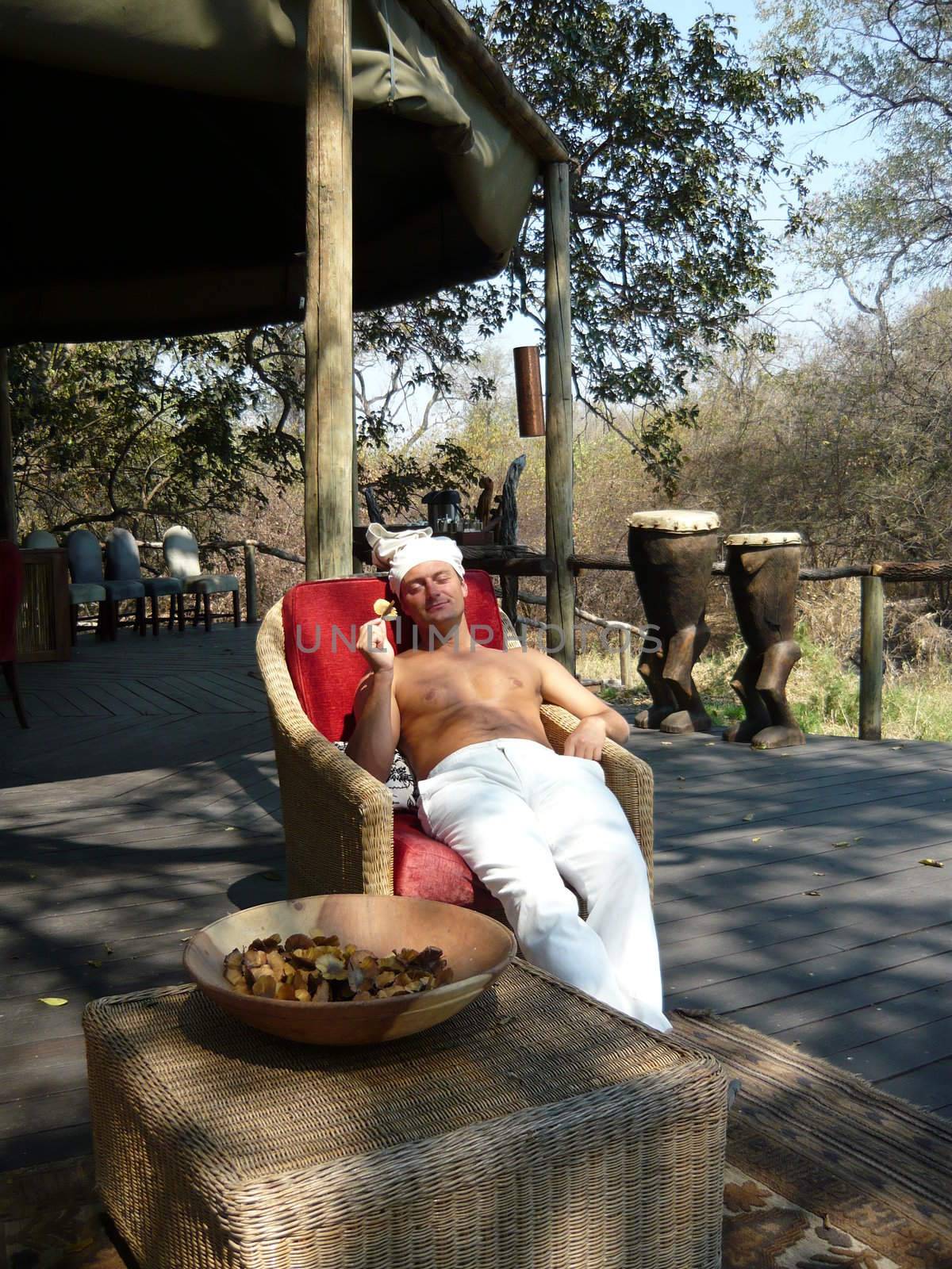 Relax. The man in the white has a rest in a wicker chair. The sun. A heat. Africa. Zambia.