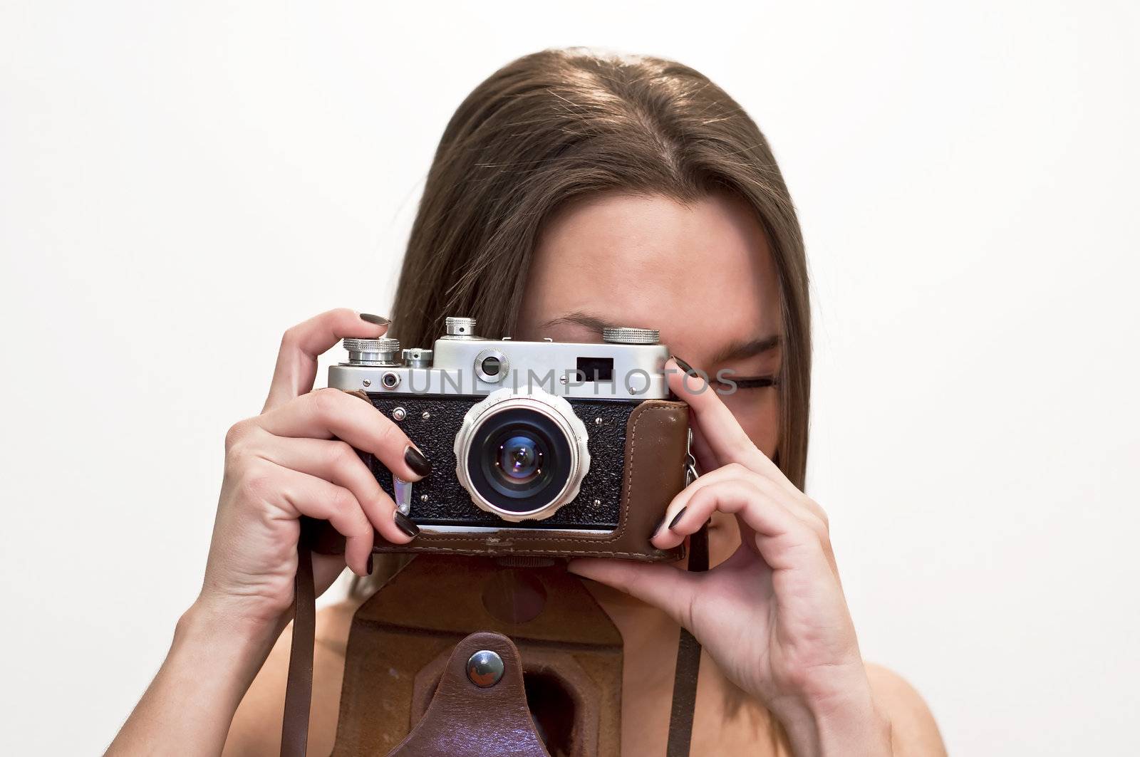 Young woman looks at an old film camera. Studio shot on white background.
