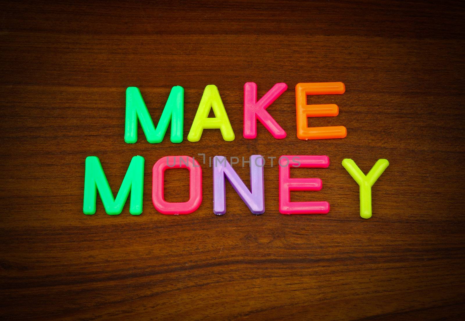 Make money in colorful toy letters on wood background  by nuchylee
