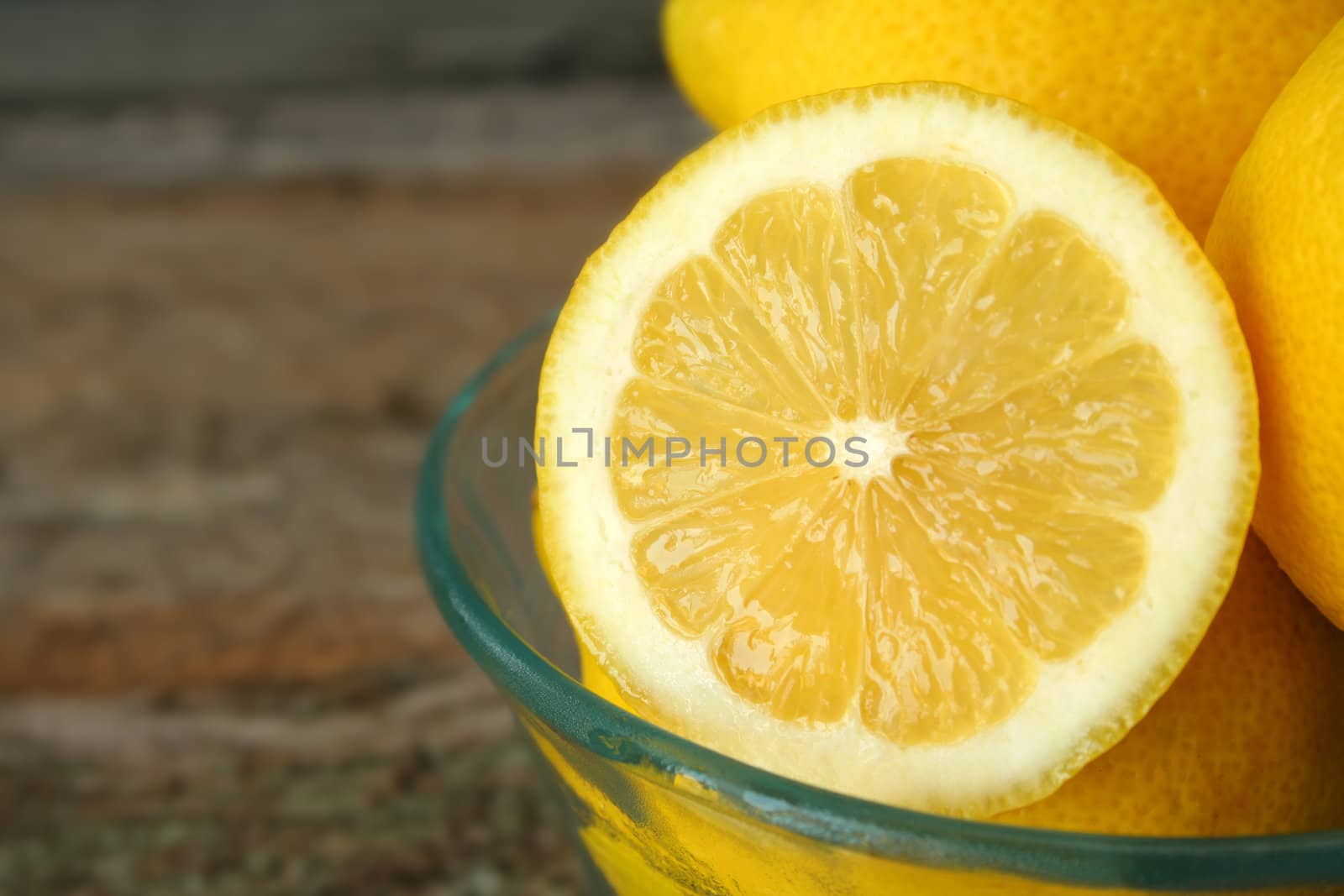 Close up of a sliced lemon in a bowl full of whole lemons.
Copy space available.