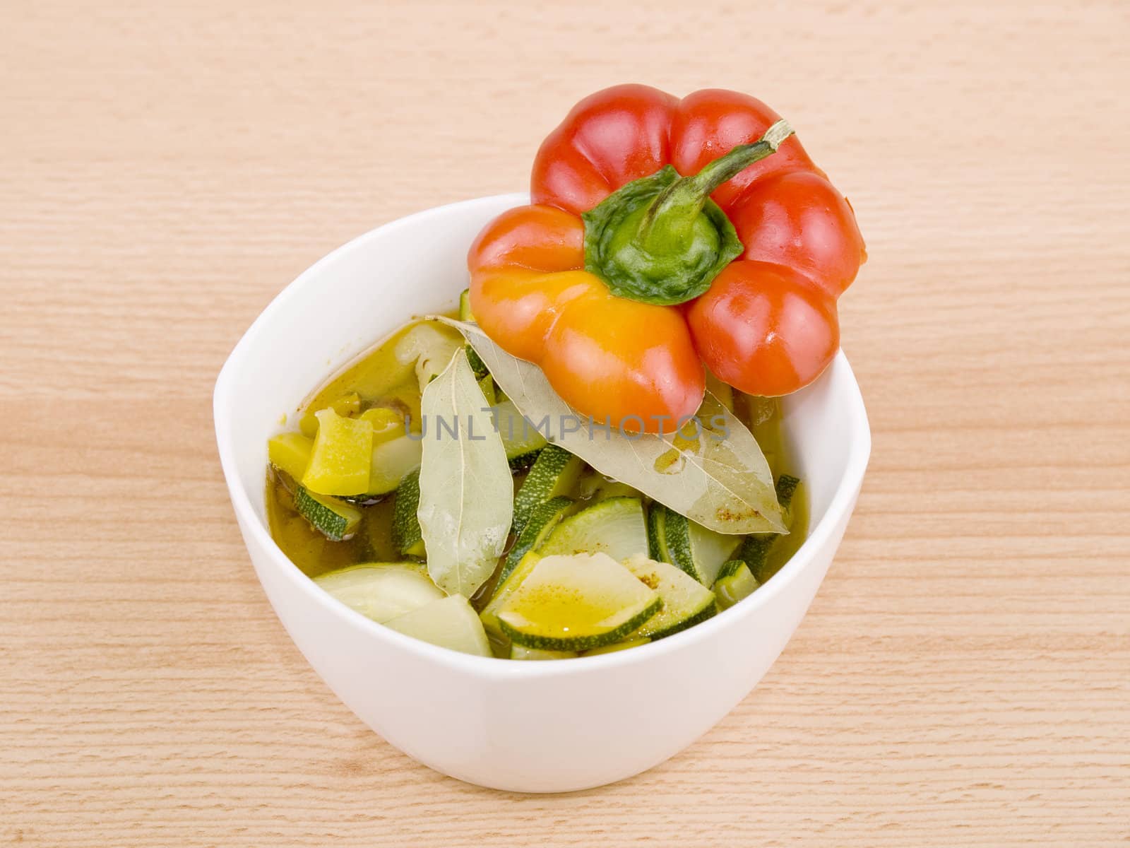 Delicious vegetarian soup made from zucchini and yellow paprika served in white porcelain bowl on wooden background