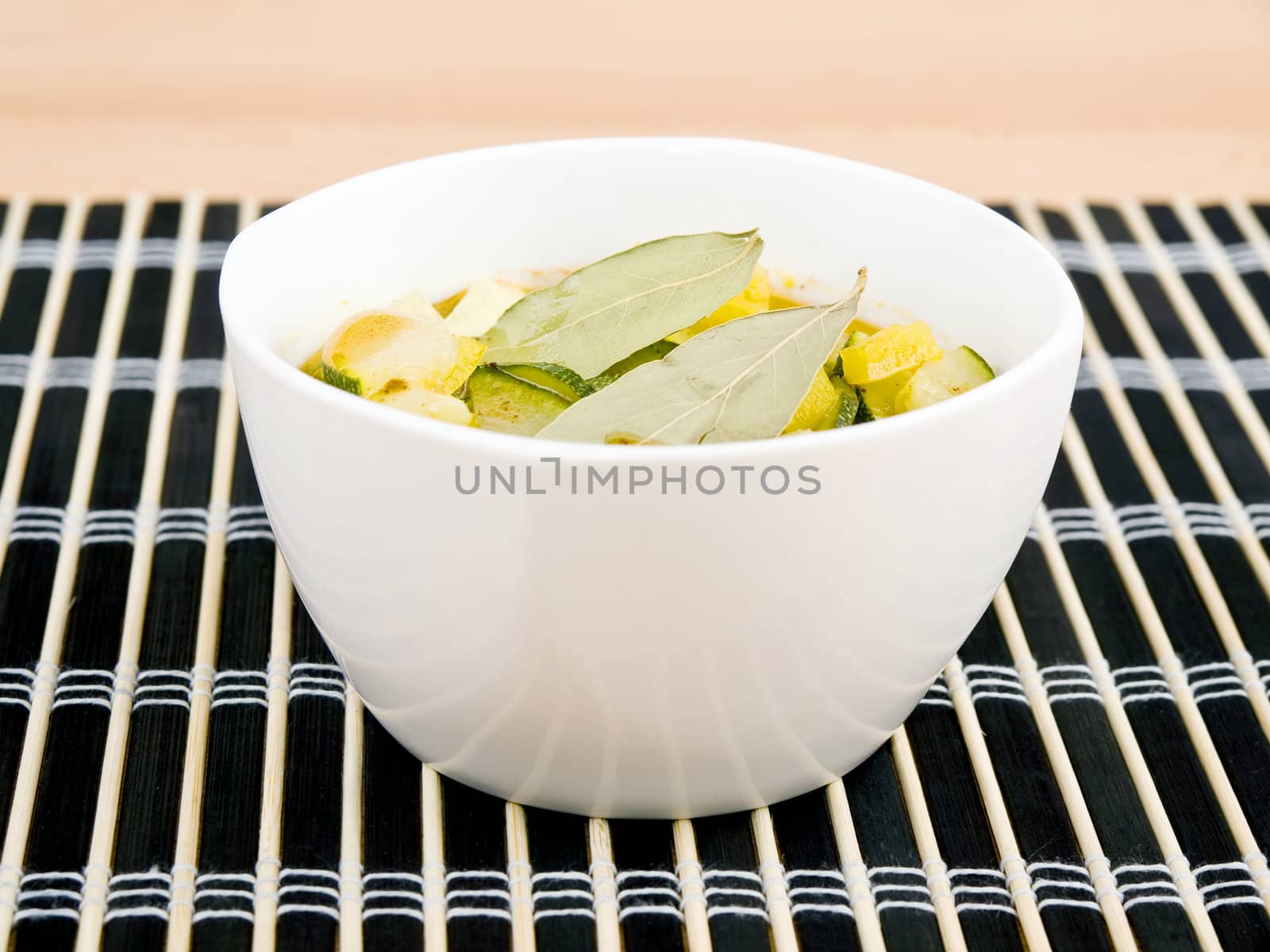 Delicious vegetarian soup made from zucchini and yellow paprika served in white porcelain bowl on black bamboo mat