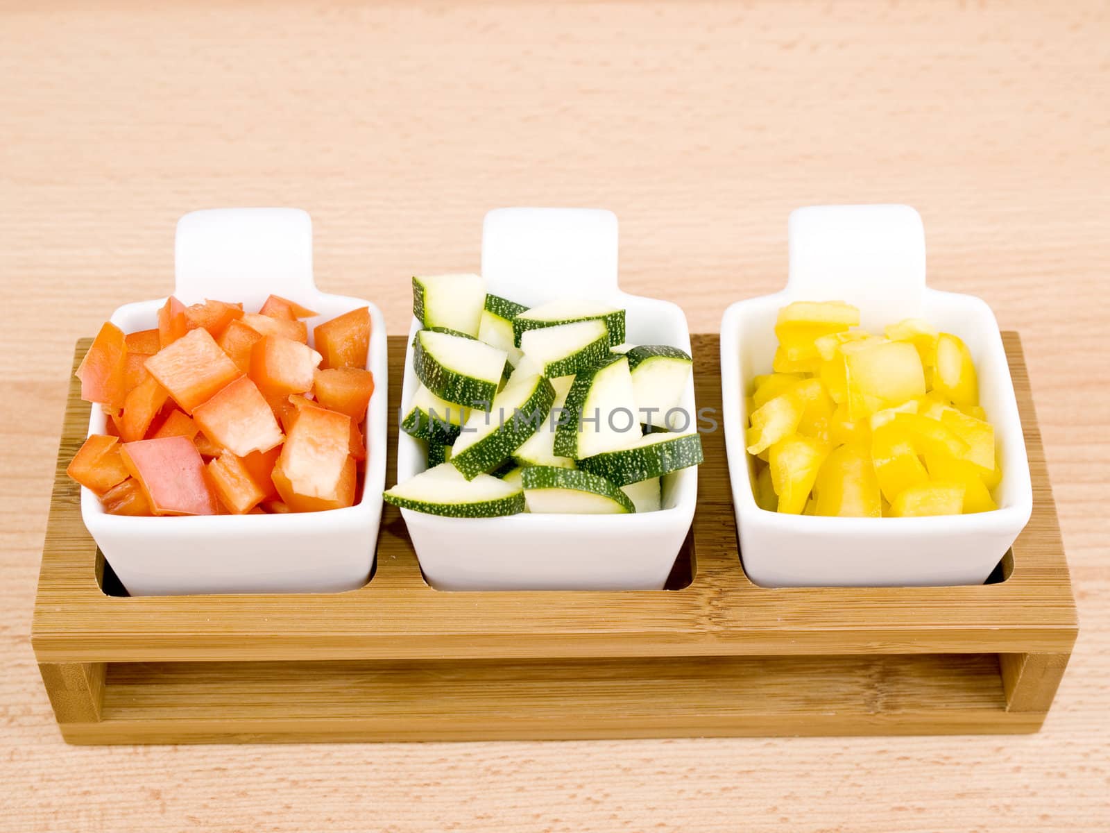 Fresh choped paprika and zucchini in small porcelain bowls on wooden table