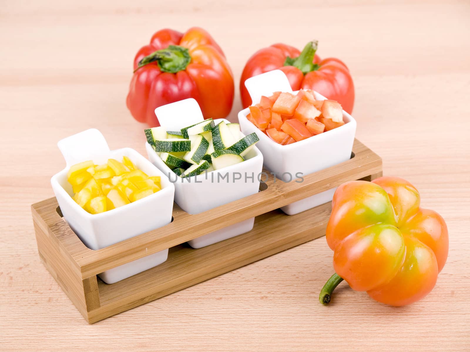 Fresh choped paprika and zucchini in small porcelain bowls on wooden table