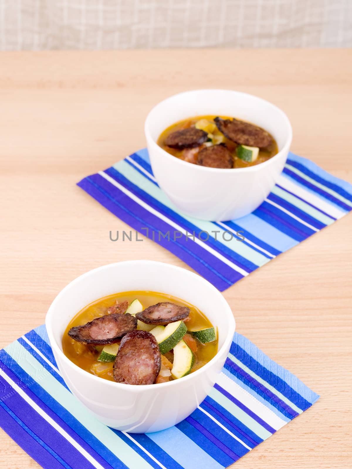 Tasty red paprika soup in white porcelain bowl on wooden background