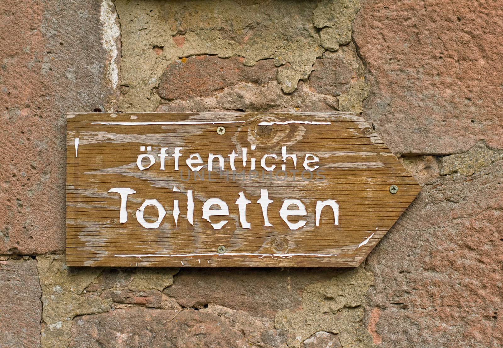 A wooden sign of public toilets WC restroom on a stone wall