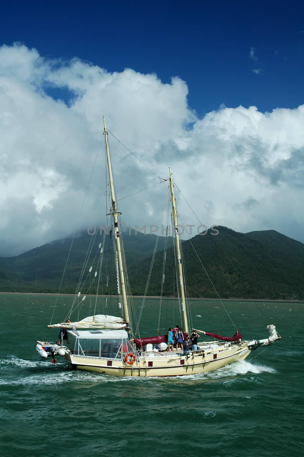 white yacht, green ocean, green hills in background, blue sky with clouds