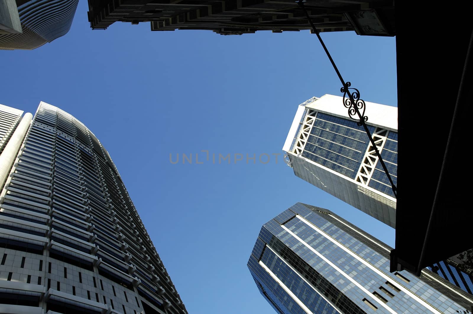 several modern skyscrapers, photo taken underneath one of them, clear blue sky