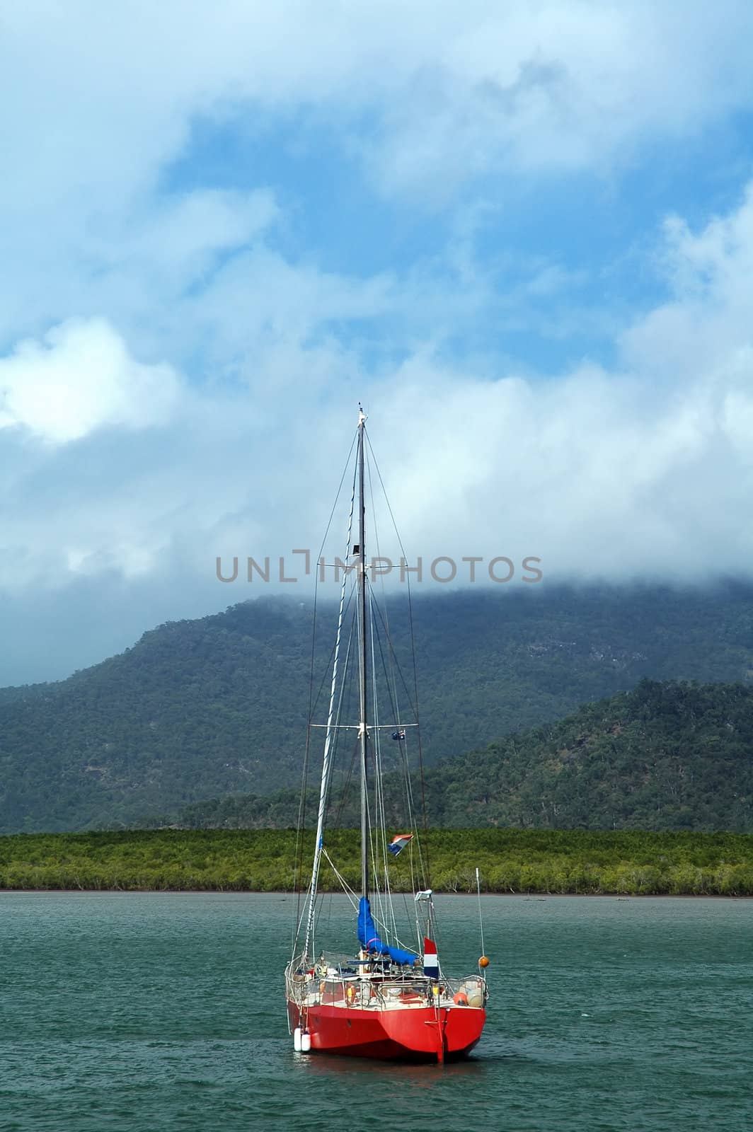 red abandoned sailboat with french and australian flags, hills in background, blue sky with clouds