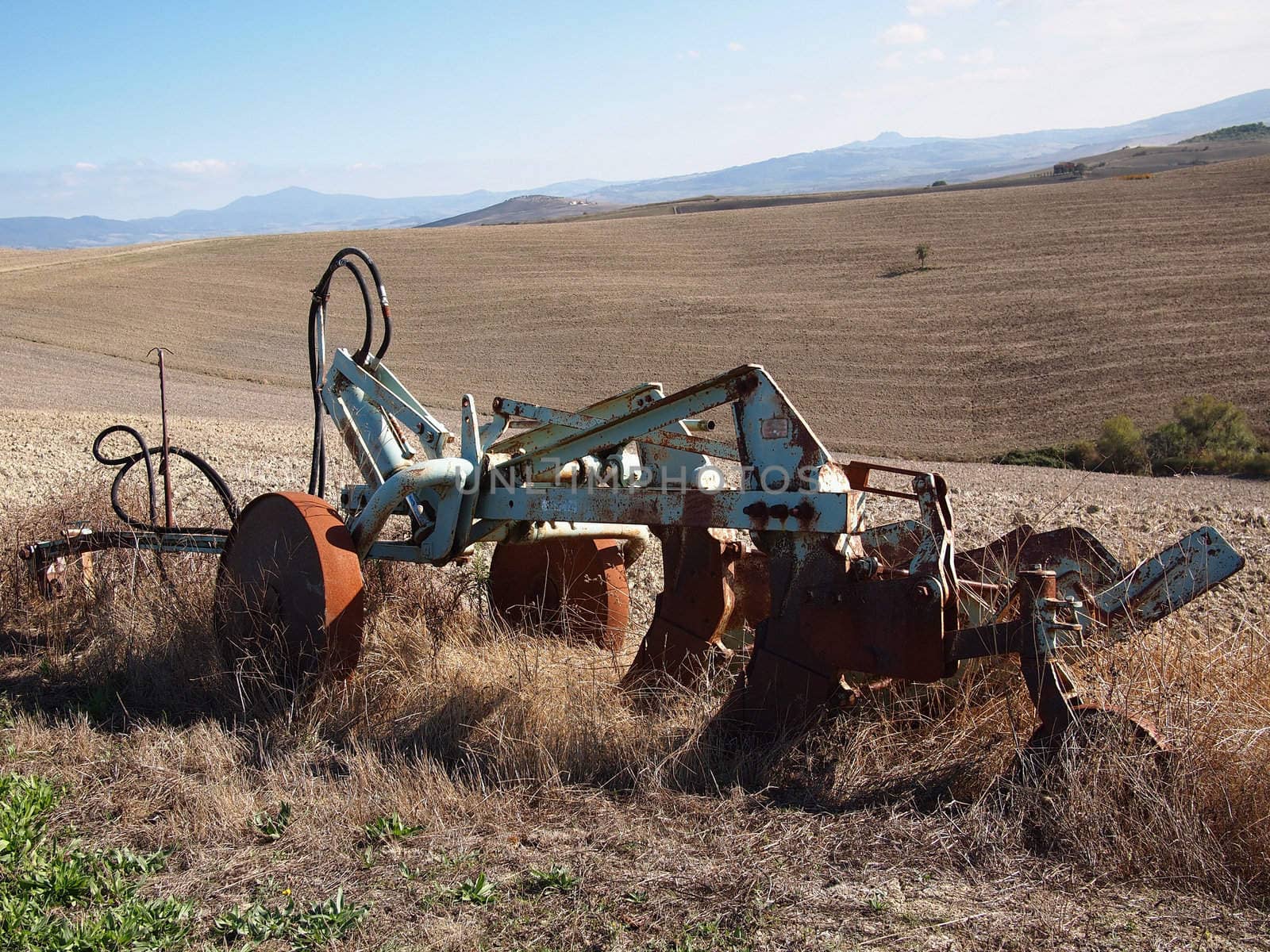 Old, rusty plough between the plowed hills of Tuscany, Italy.