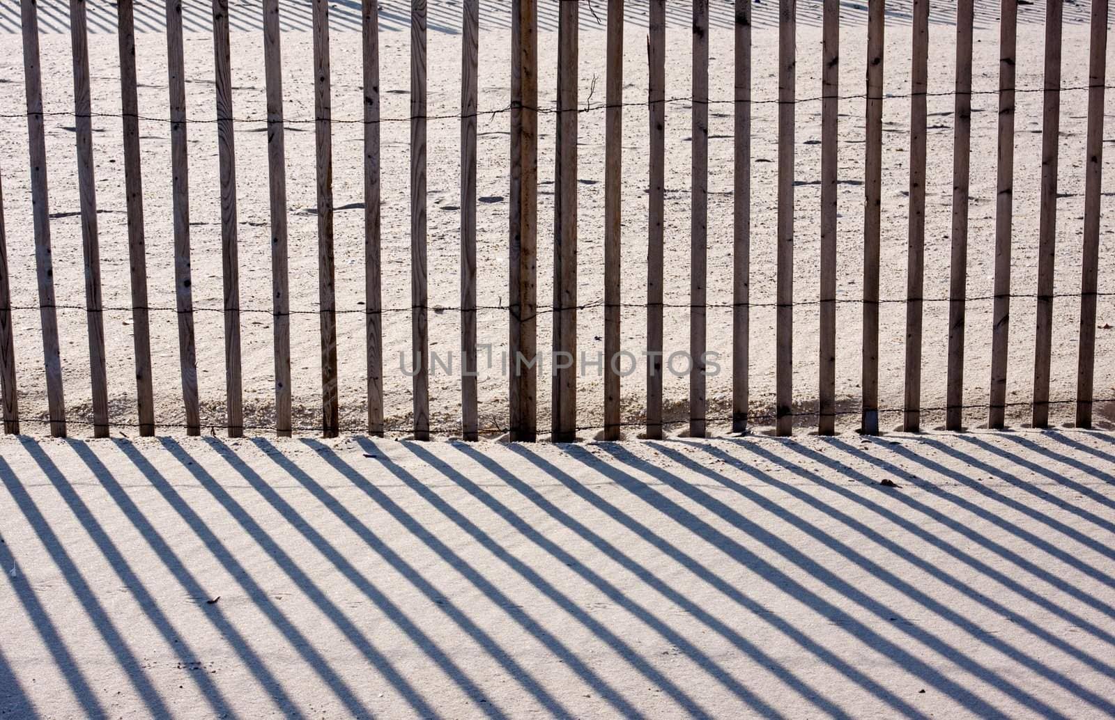 An abstract image of a fence on a beach with diagnol shadows
