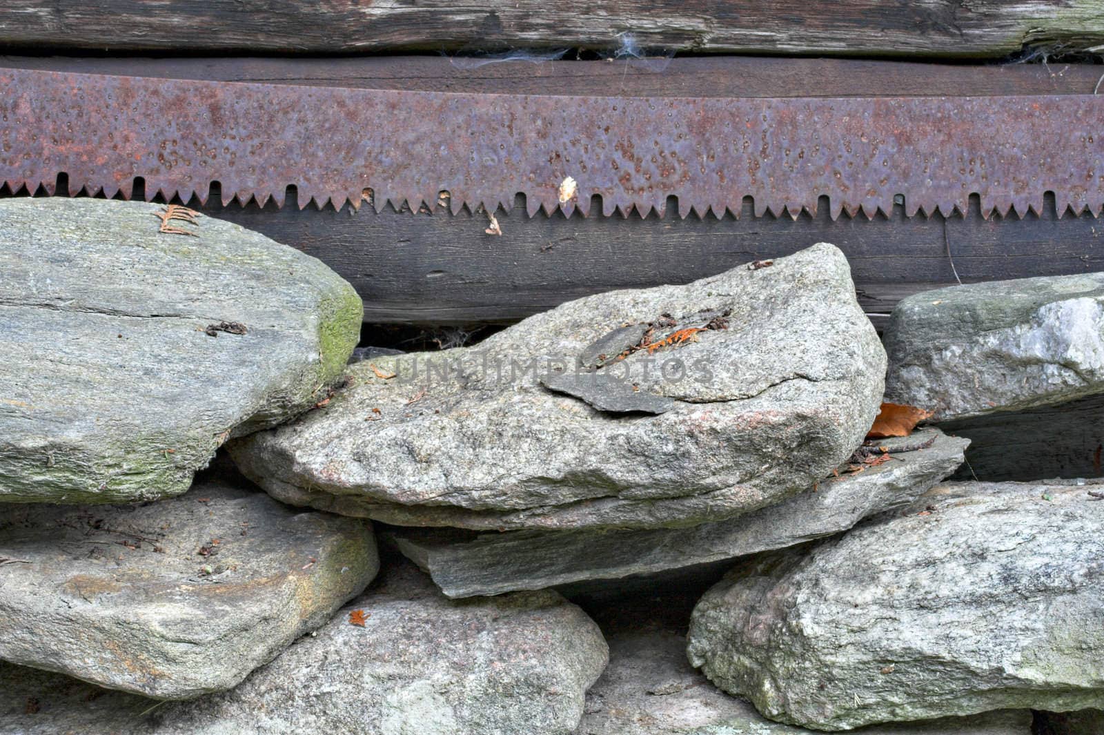 A rusty old saw blade hanging above a pile of stacked rocks.