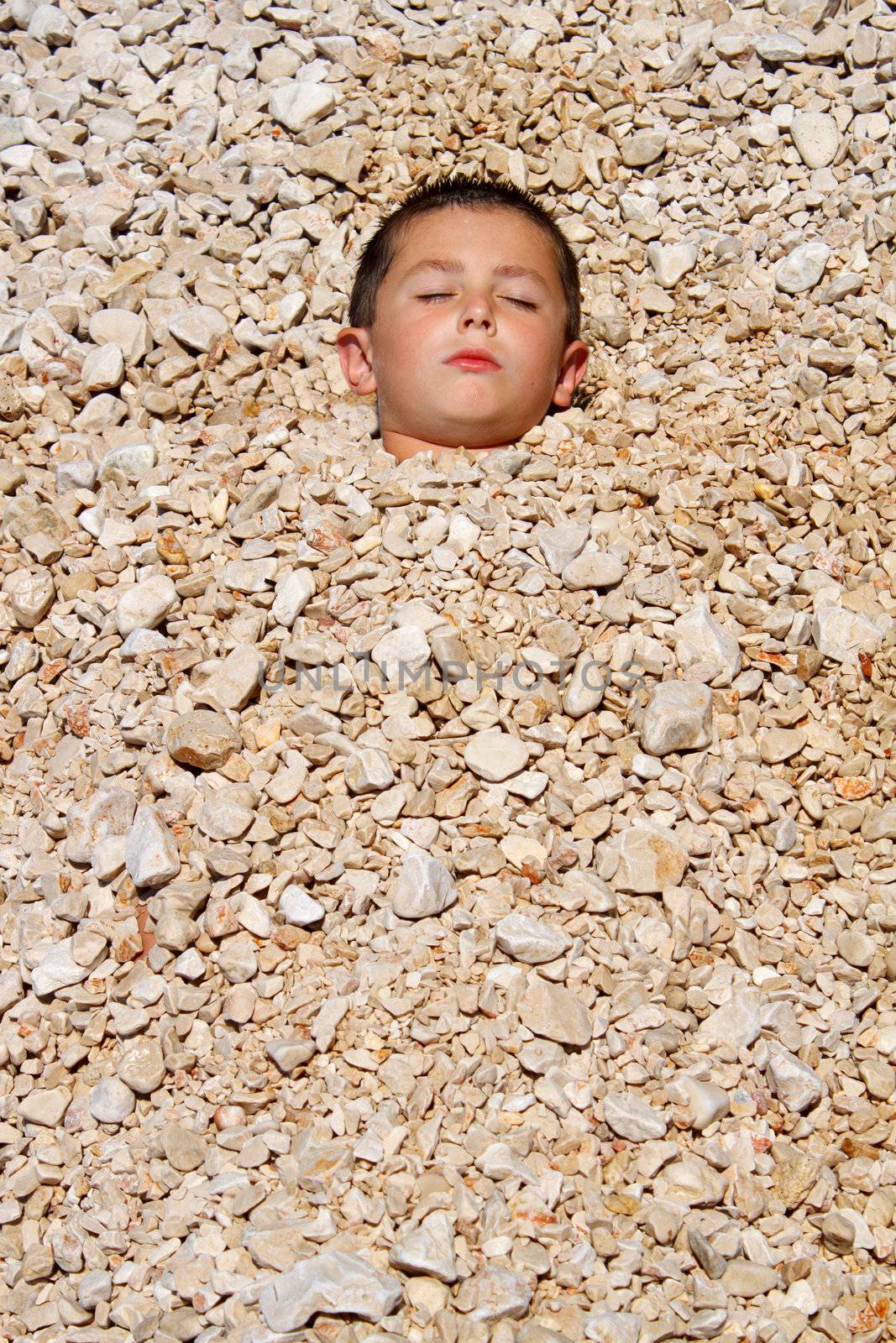 boy buried in the pebbles on the beach