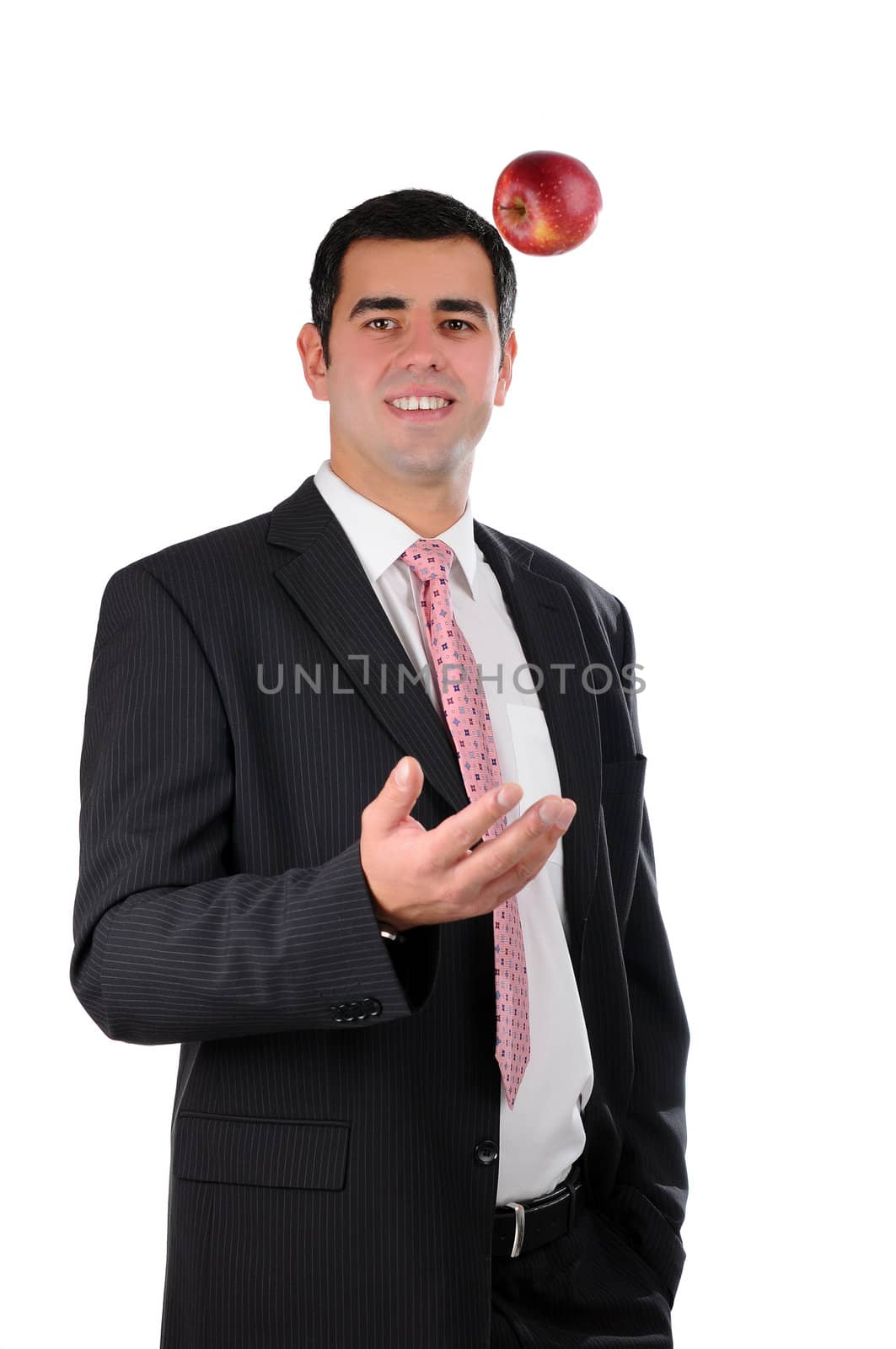 Portrait of a young cheerful businessman in a dark suit tossing an apple isolated on white