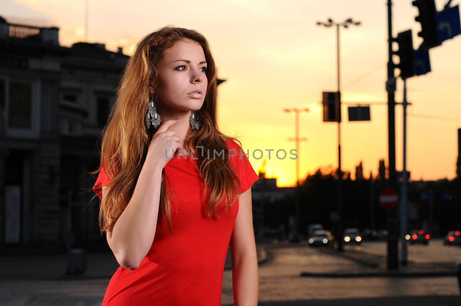 Portrait of a young attractive woman in a red dress in the city at dusk