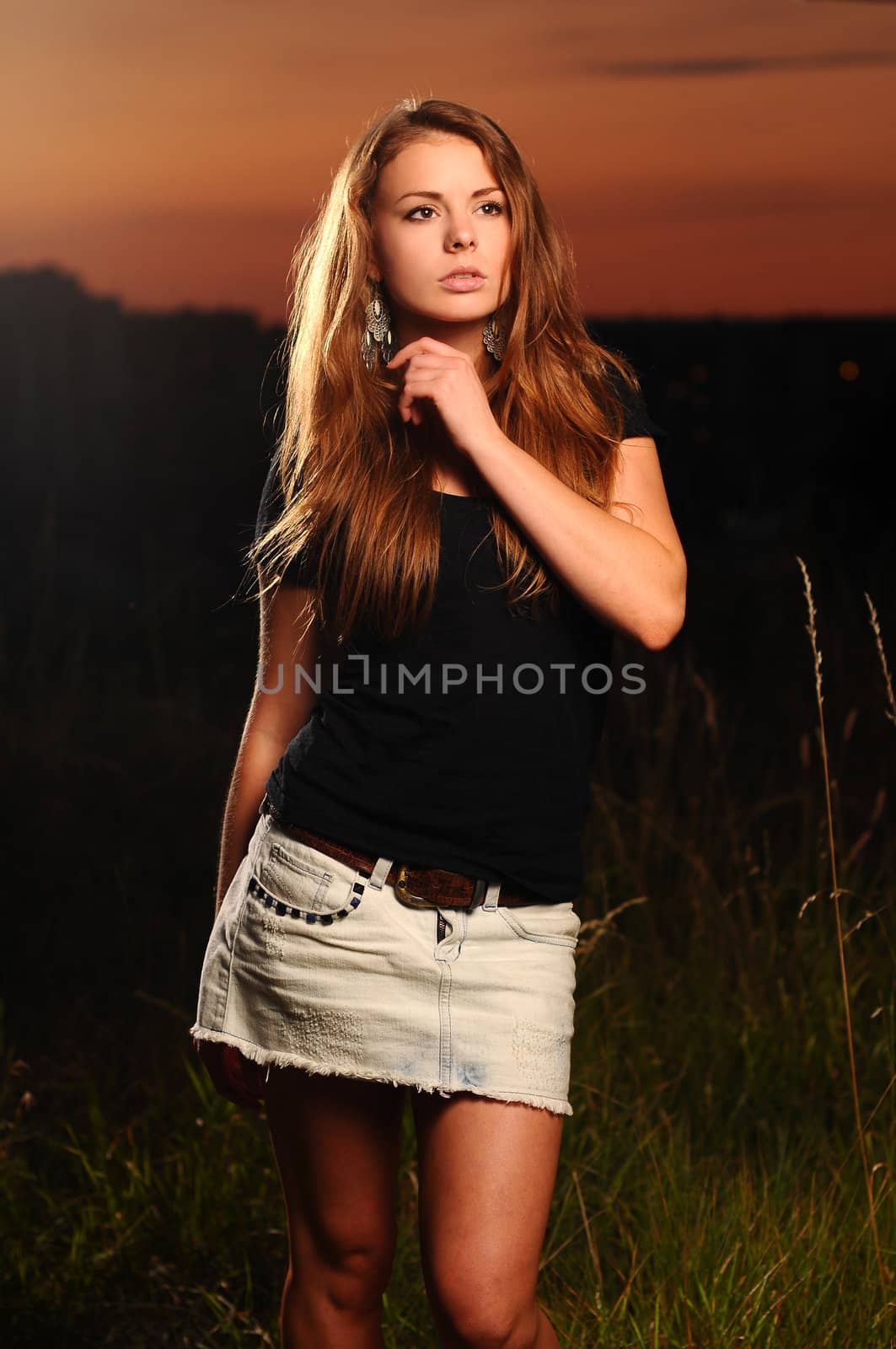 Portrait of a young attractive woman in a black shirt and jeans skirt at dusk