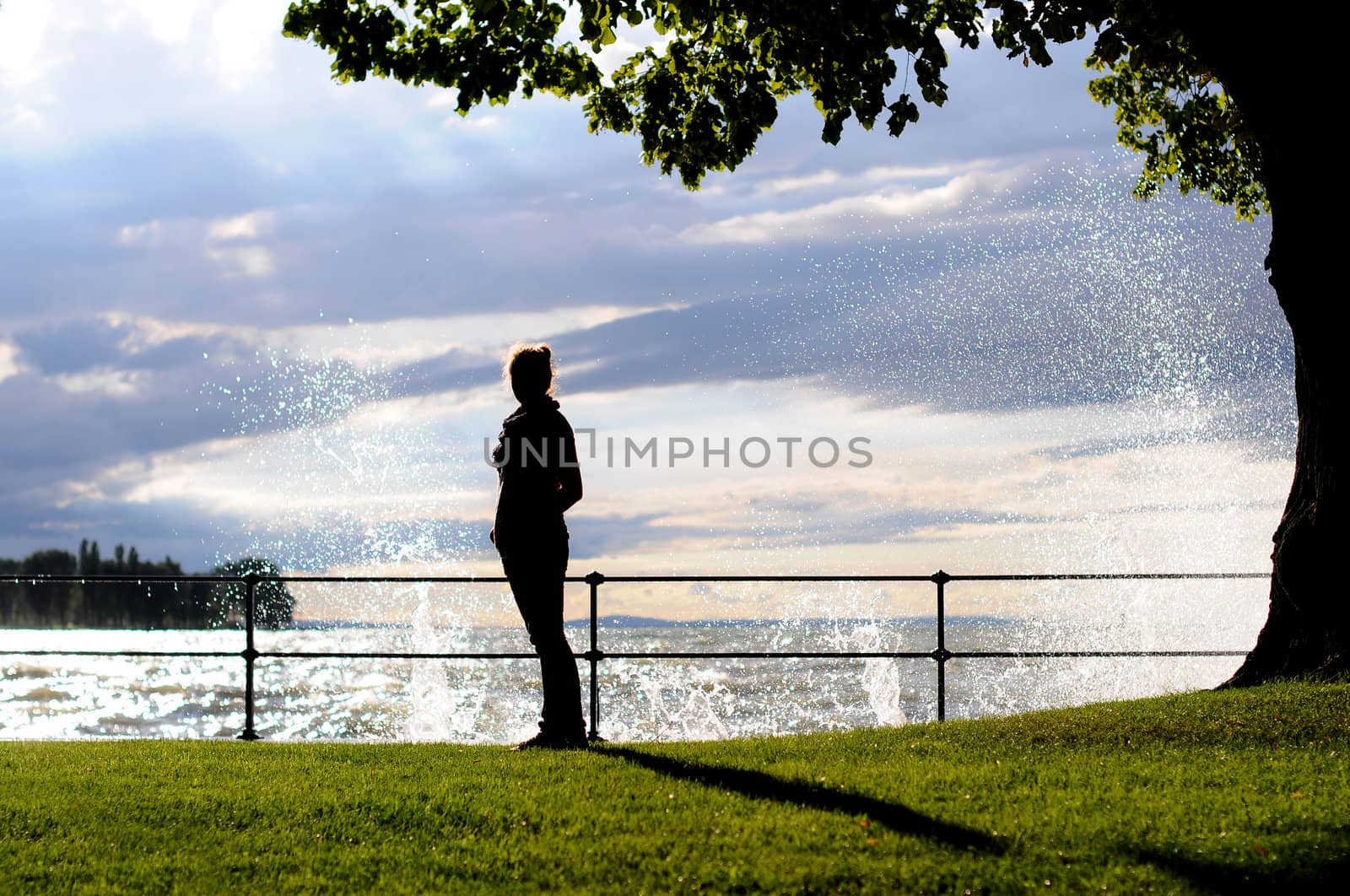 Silhouette of a young woman at the seaside standing on grass with water splashes behind by gravityimaging1