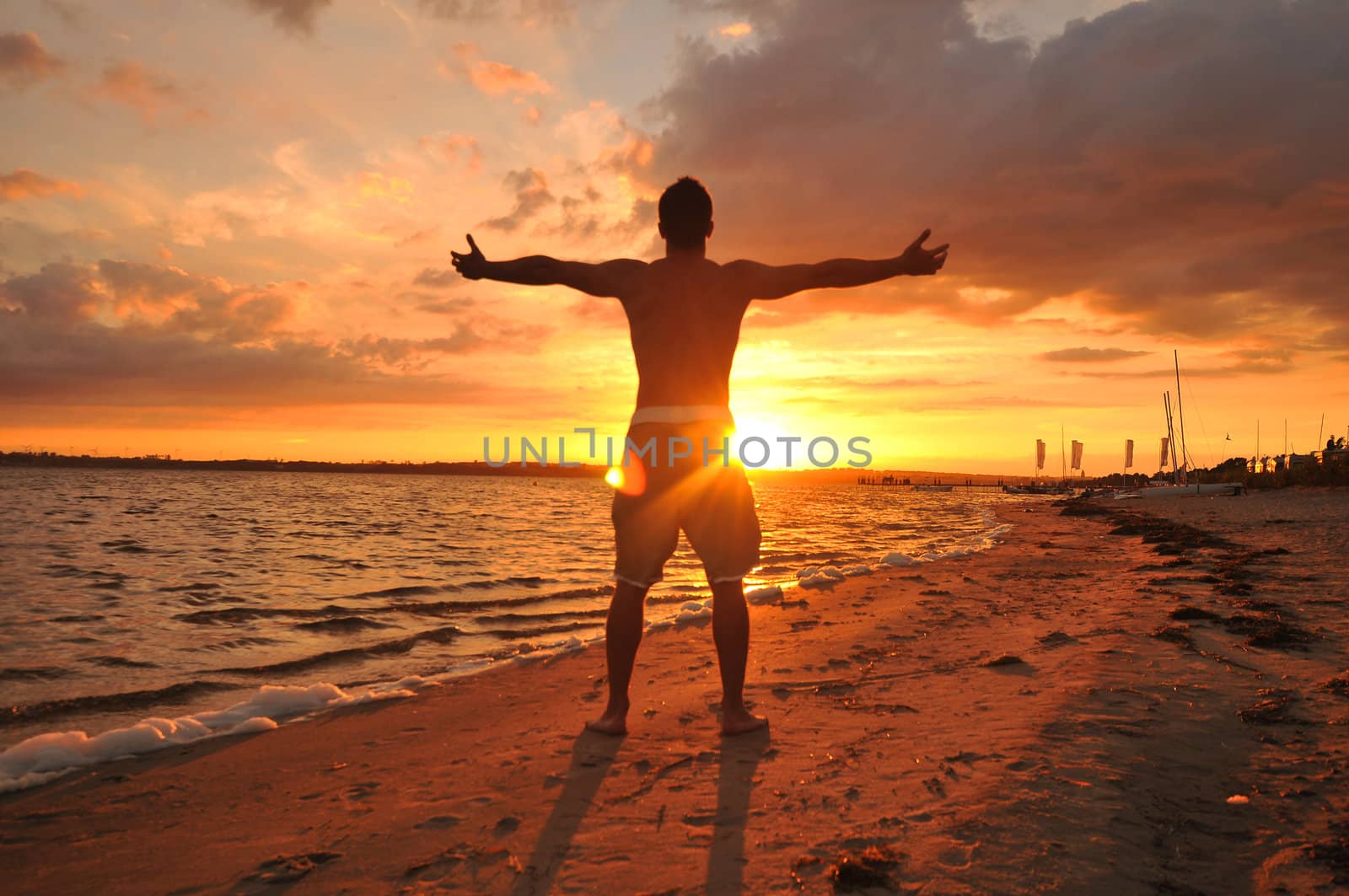 Young man with spread arms celebrating and enjoying the moment at the seaside at sunset