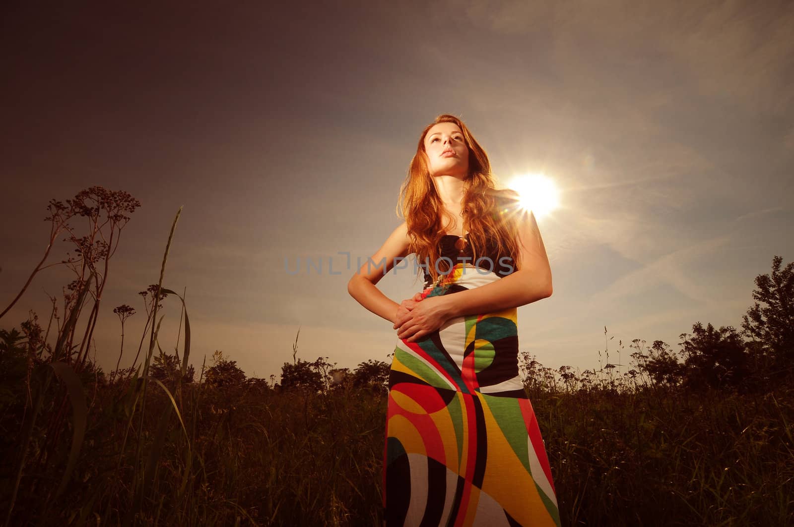 Portrait of a young attractive woman in a colorful dress posing in the sun outdoors