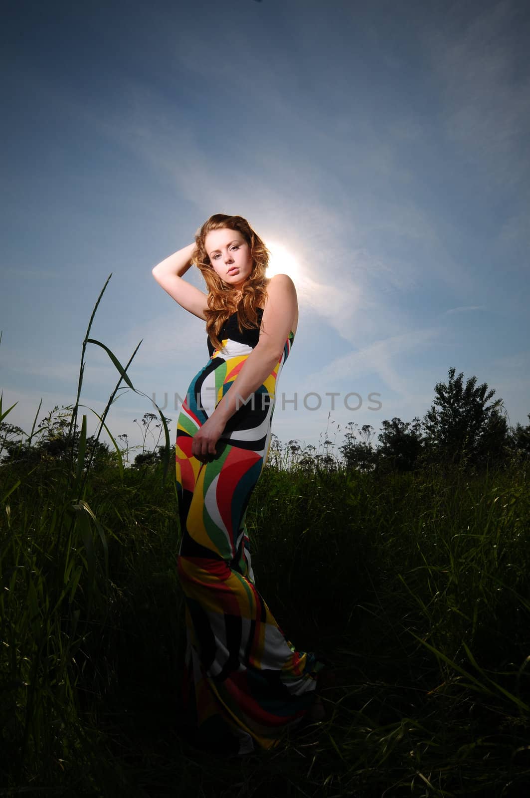 Portrait of a young attractive woman in a colorful dress posing in the sun outdoors by gravityimaging1