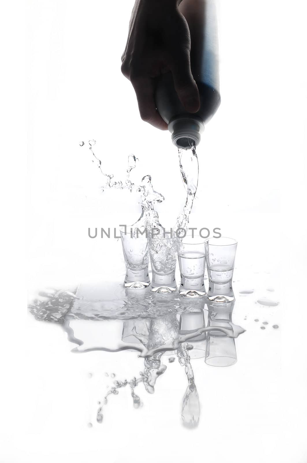 Pouring water or alcohol drink froma a bottle into glasses on white background