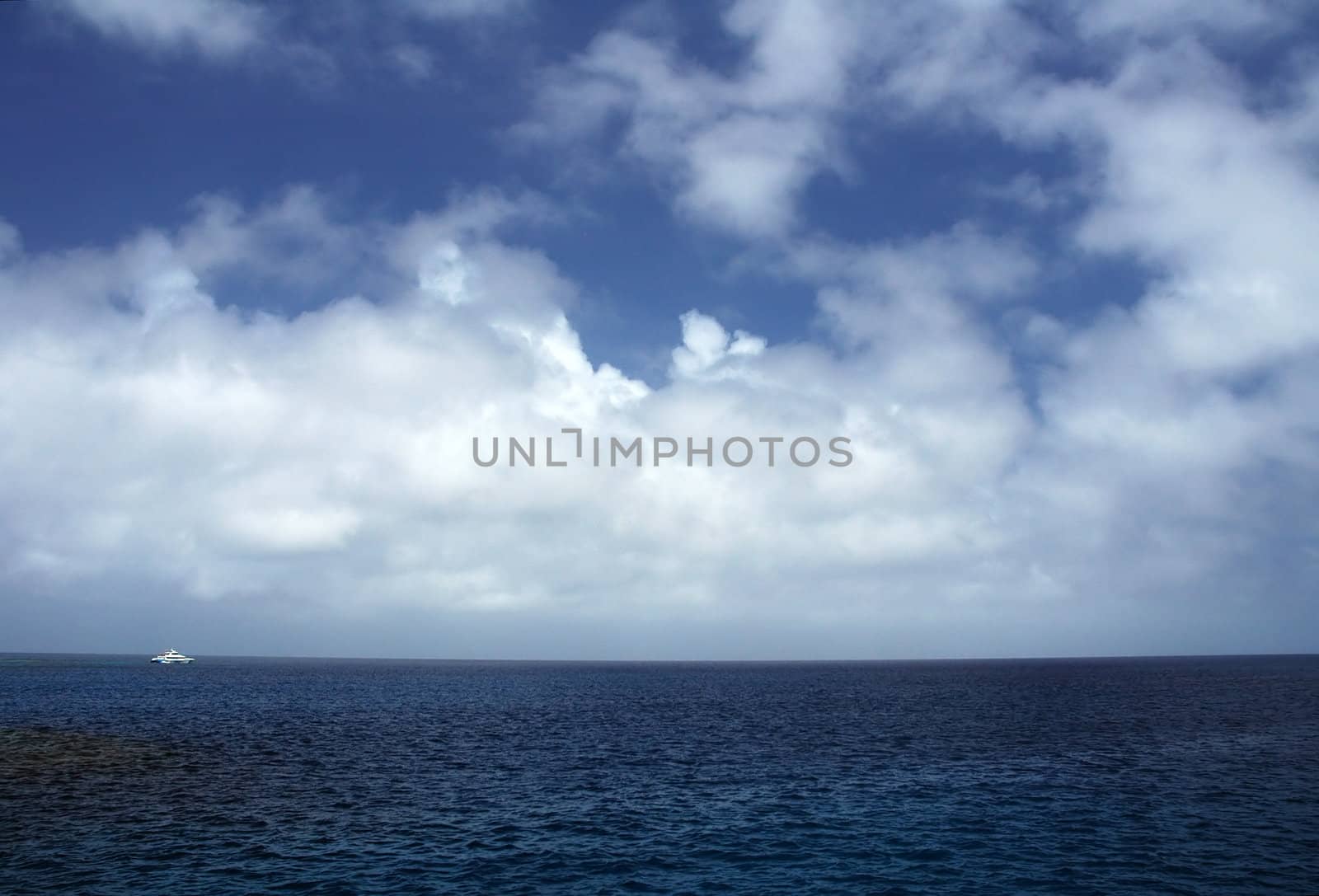ocean scenery, blue sky with clouds, white boat in distance, location: Great Barrier Reef, near Cairns