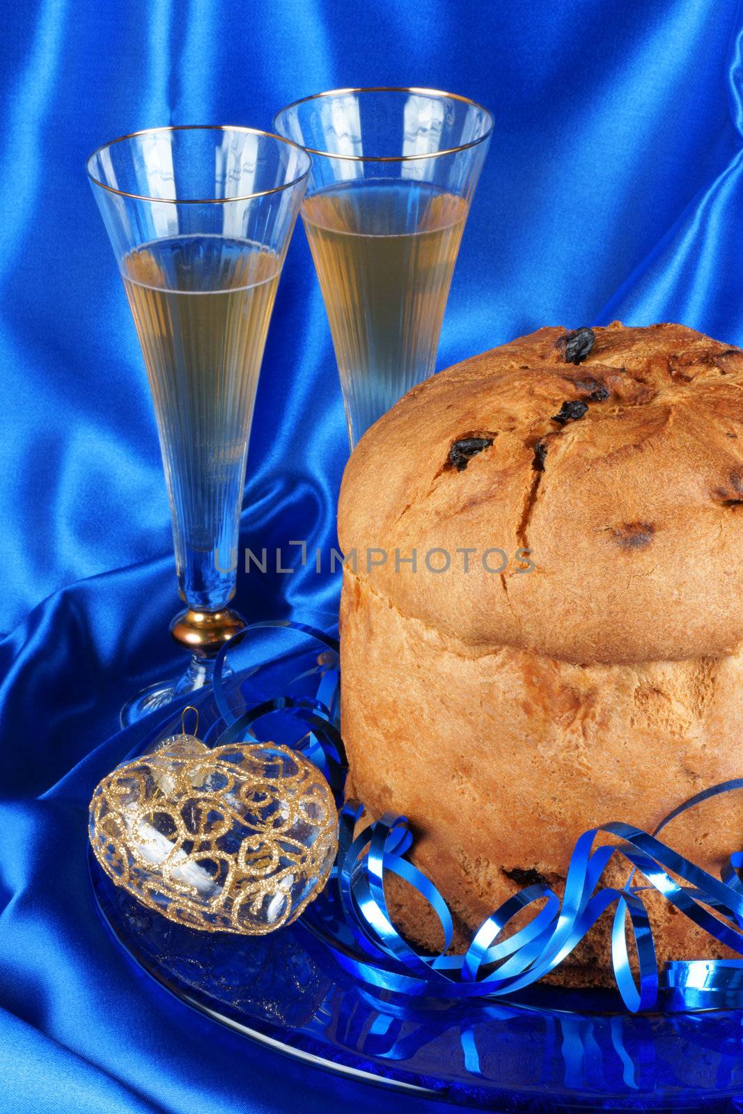 Panettone the italian Christmas fruit cake served on a blue glass plate over a yellow background and two glasses of spumante (sparkling wine). Selective focus.