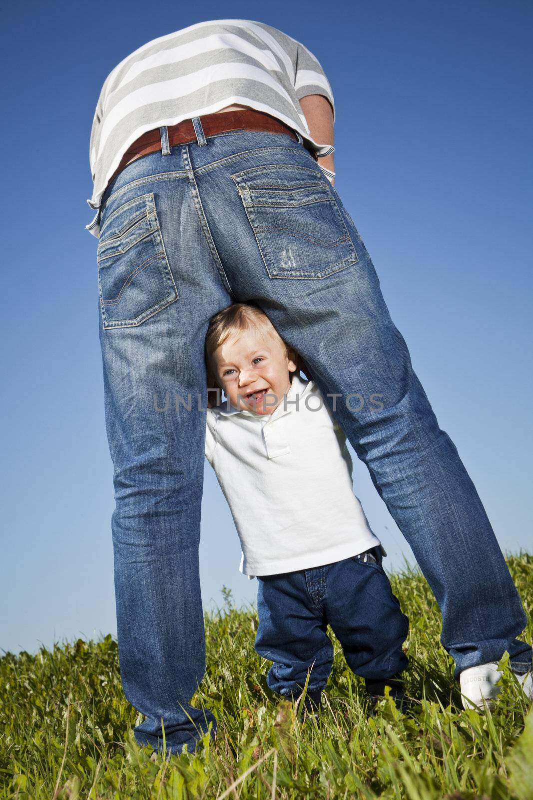 Young boy playing around his fathers legs