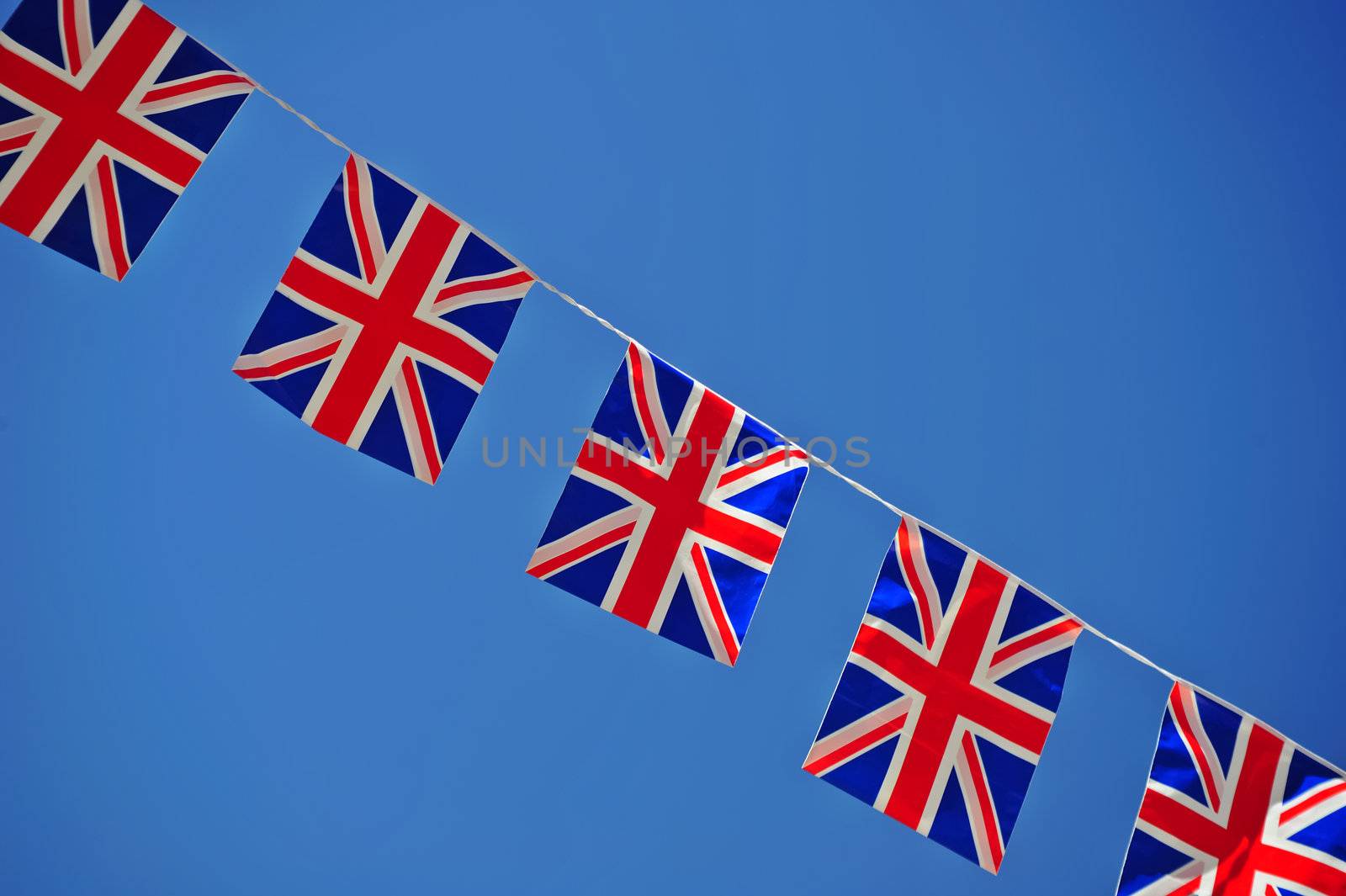 A line of Union ack flagy, stetched across a clear blue sky. Space for text either side of the flags