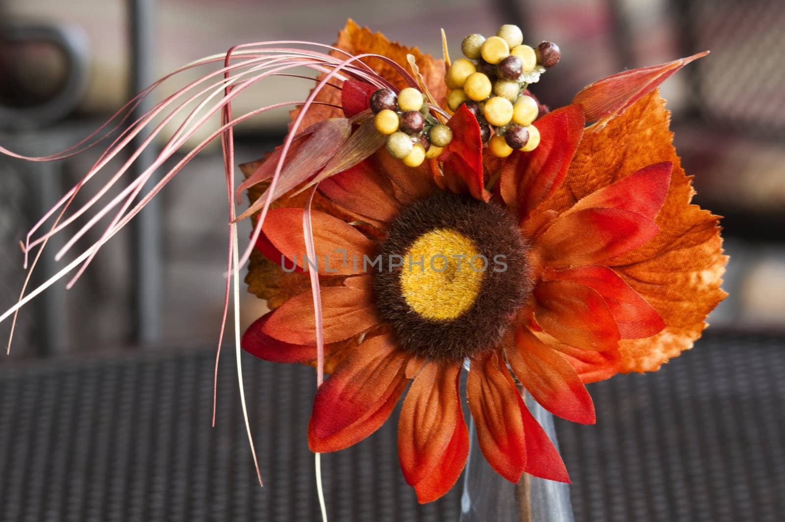 Bright orange silk flower in a small, single bloom arrangement brings a simple touch of nature's color to a patio table