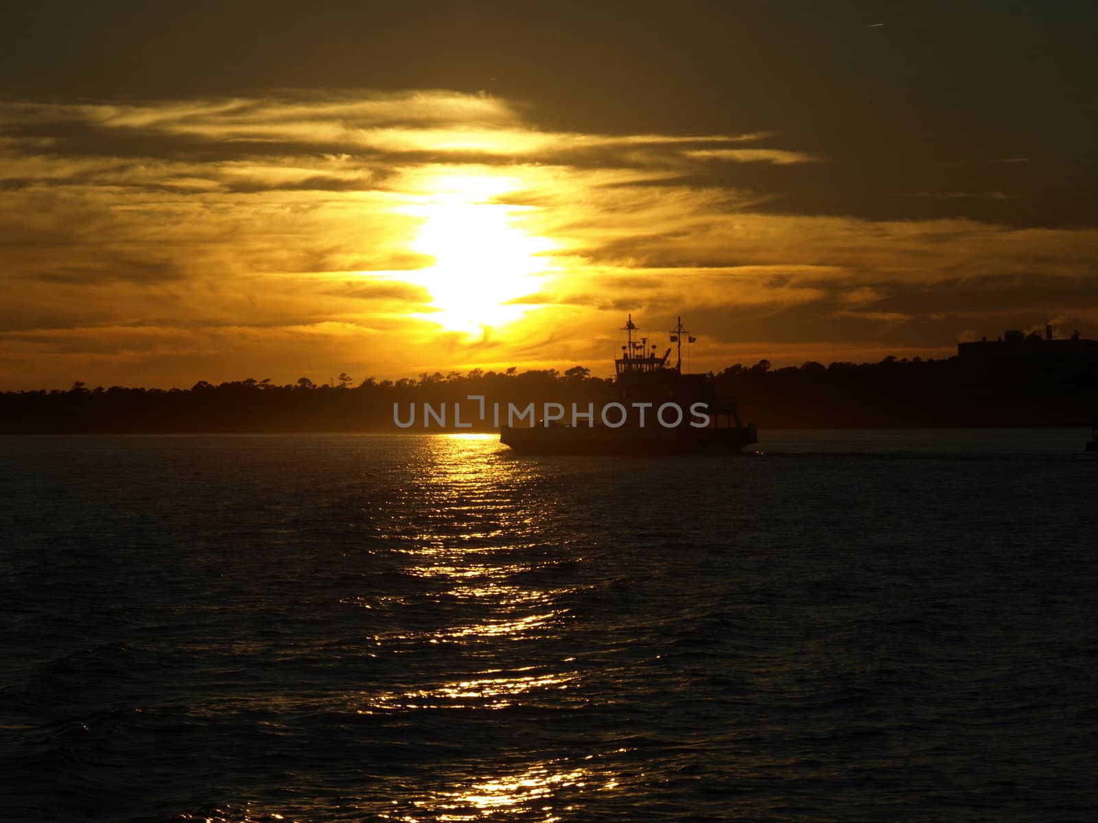 A ferry boat crosses the water against the setting sun