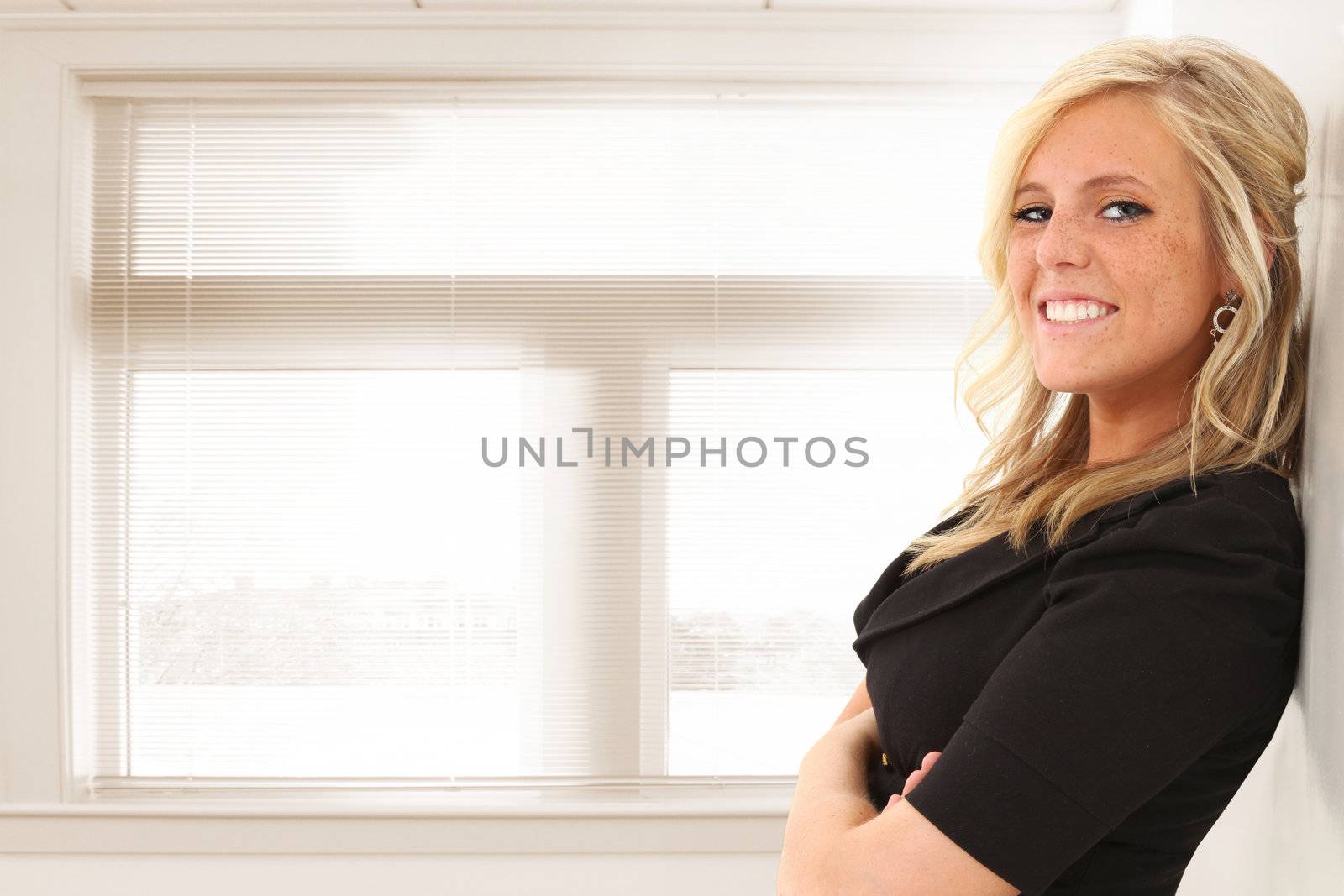 Beautiful young blond woman standing in front of window at office or school.  Space for copy.