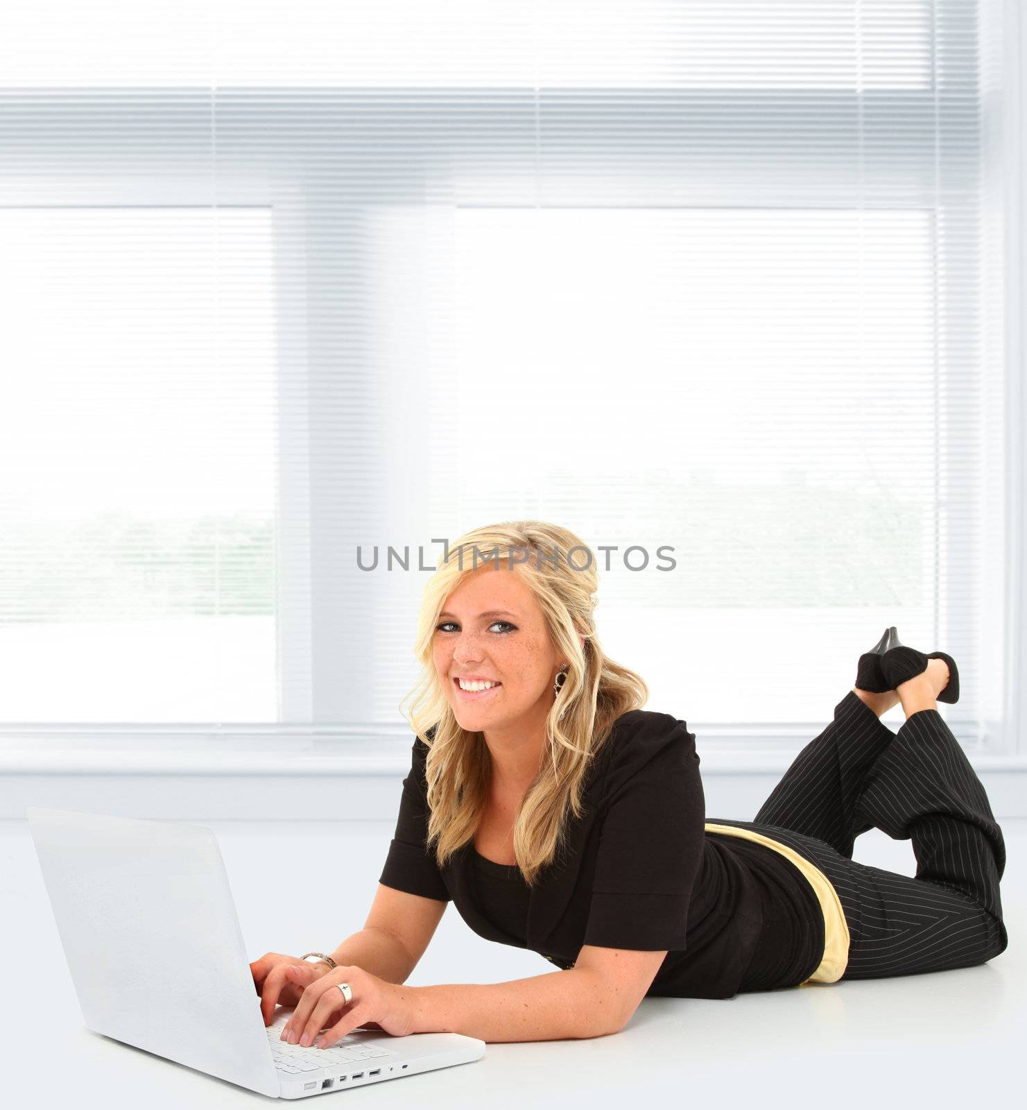 Beautiful young woman working on laptop in school or office on floor with copy space.