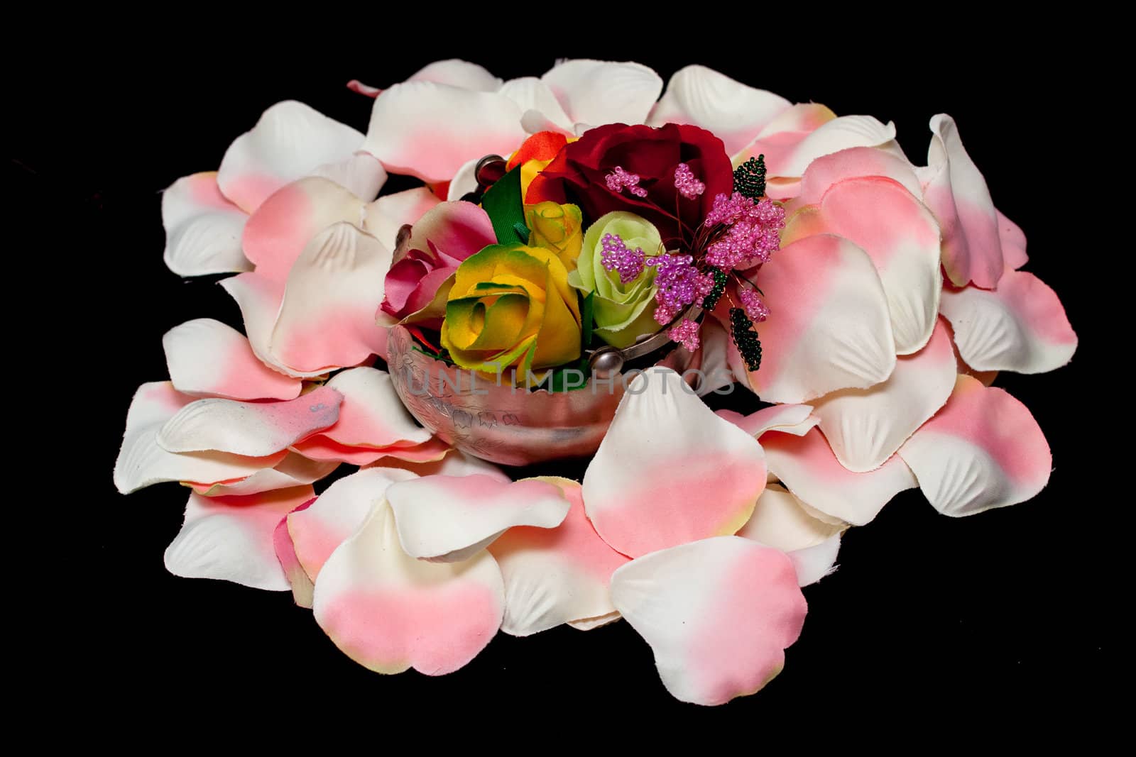 A silver basket with artificial roses on white and pink rose textile petals on black
